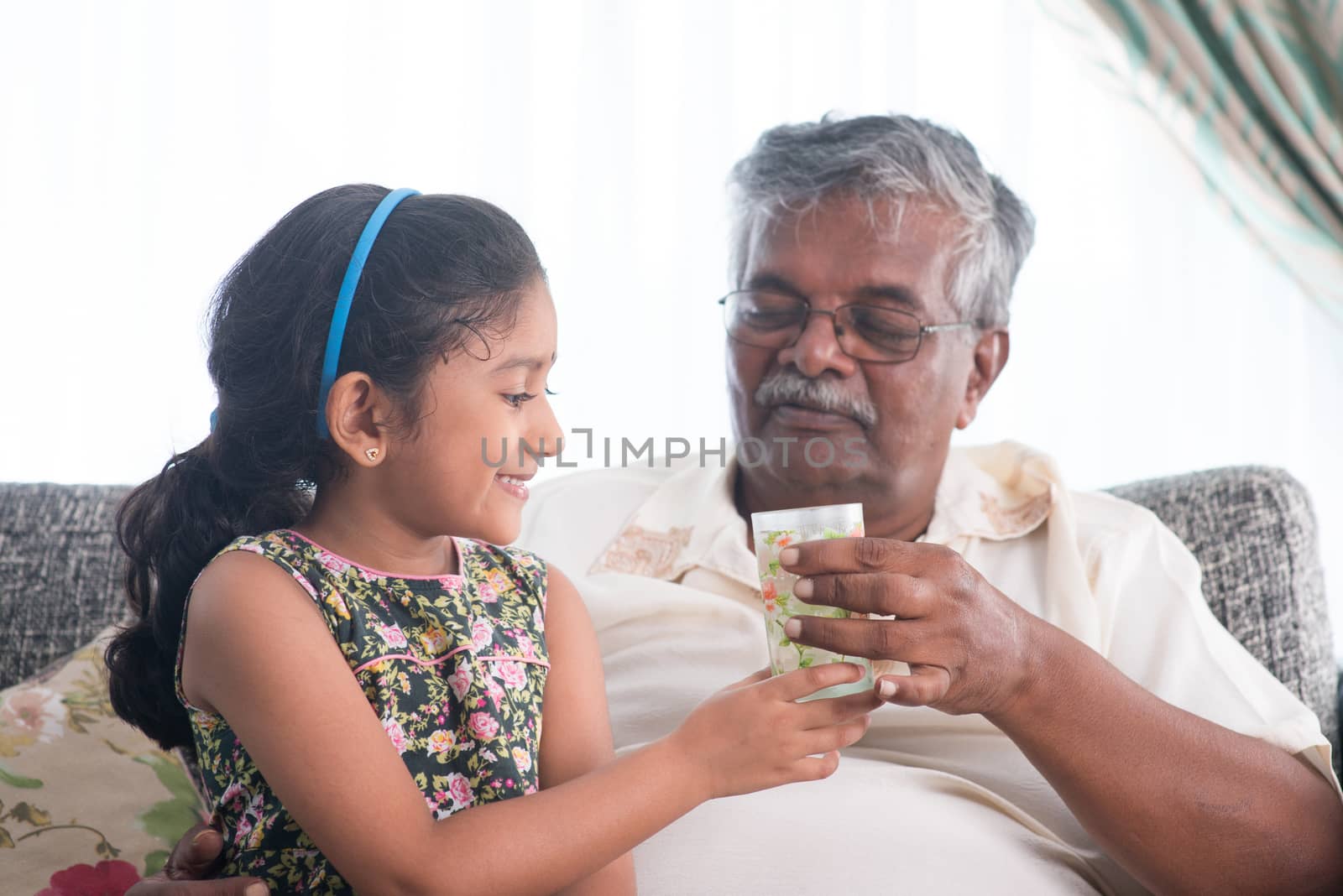 Portrait of Indian family at home. Grandchild giving a glass water to grandparent . Asian people living lifestyle. Grandfather and granddaughter.