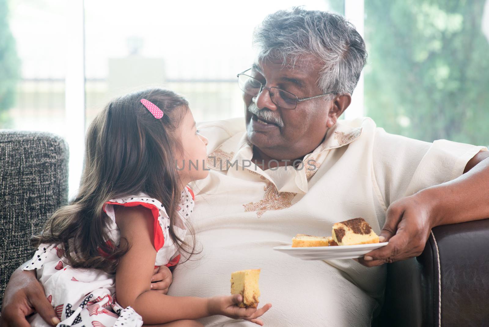 Portrait of Indian family at home. Grandparent and grandchild eating butter cake. Asian people living lifestyle. Grandfather and granddaughter.