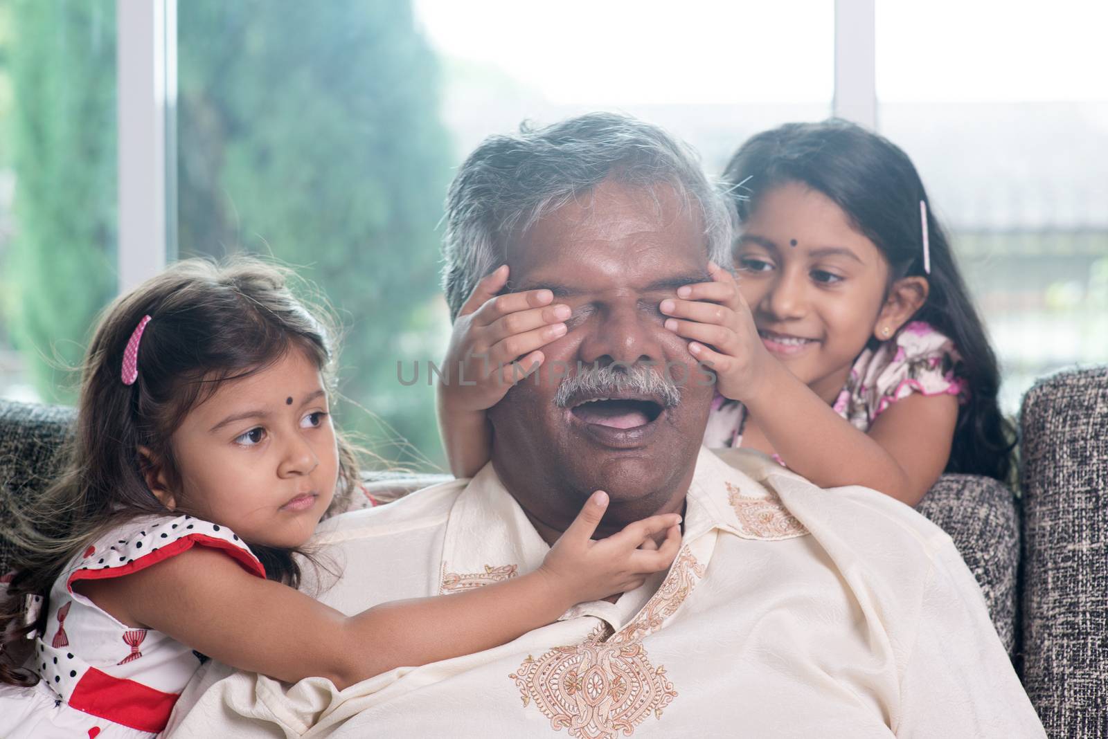 Happy Indian family at home. Asian girl surprising her father by covering daddy eyes. Parent and child indoor lifestyle.