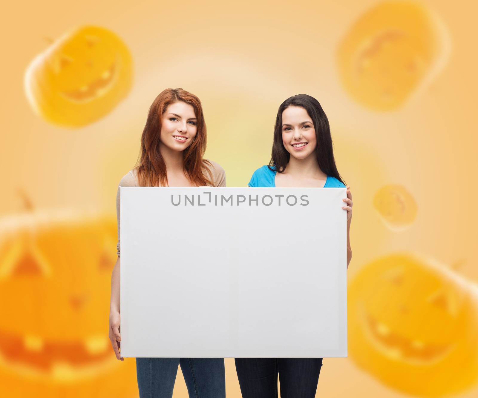 advertising, education, holidays and people concept - smiling teenage girsl with white board over halloween pumpkins background