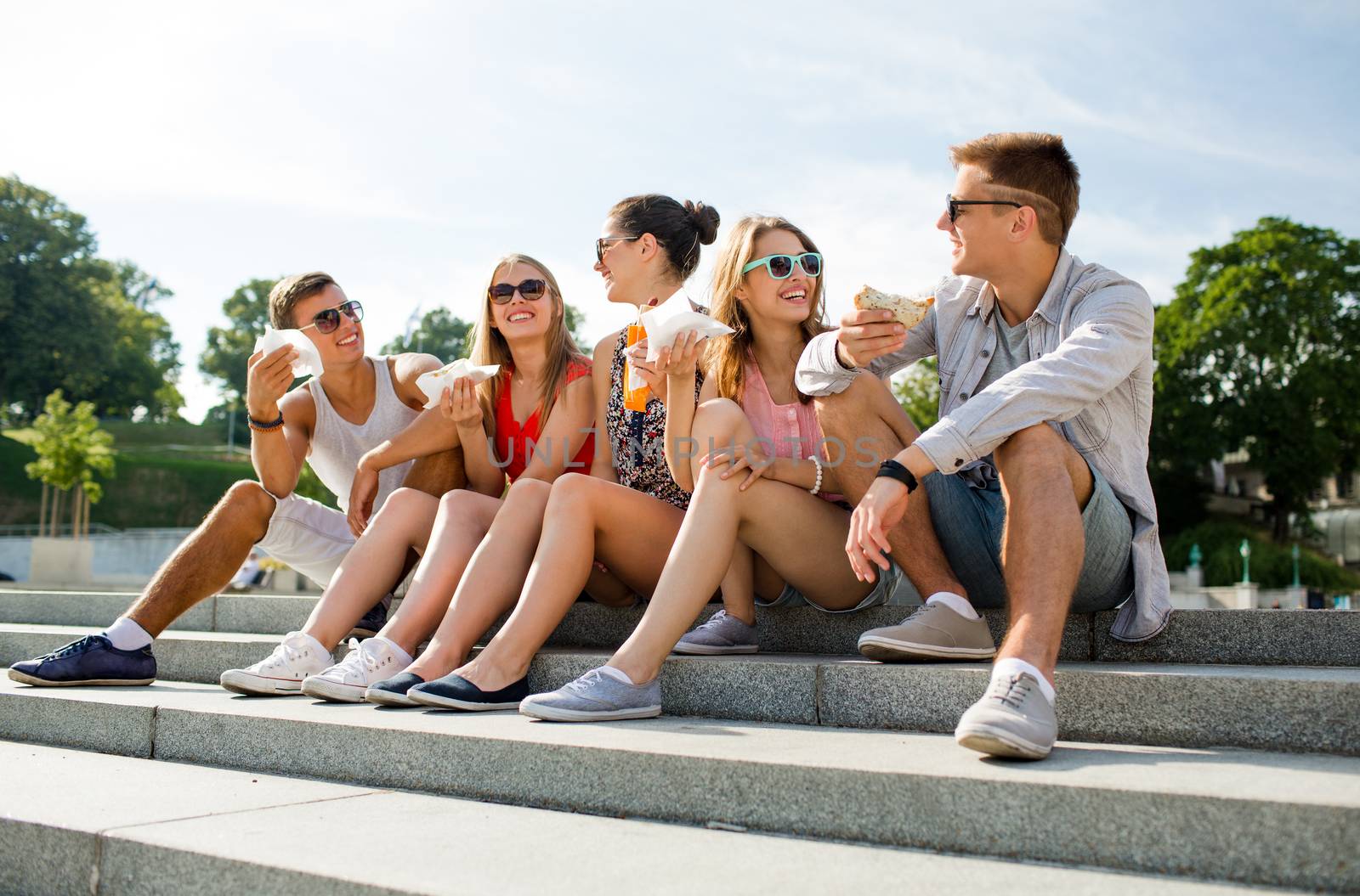 group of smiling friends sitting on city square by dolgachov