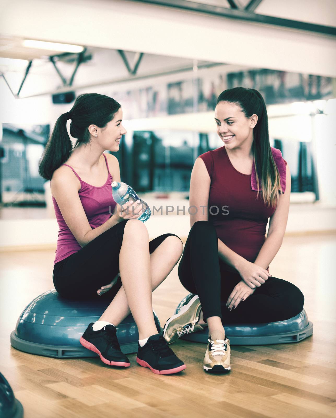 fitness, sport, training, gym and lifestyle concept - two smiling women sitting on the half ball and relaxing after class in the gym