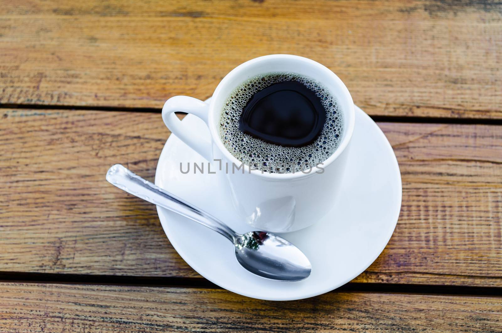 Cup of coffee with a white plate standing on a wooden table.