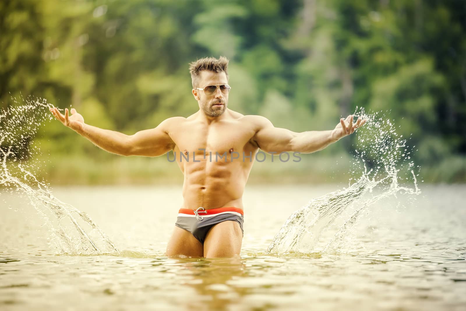 An image of a muscular man in the lake with a white shirt and sunglasses