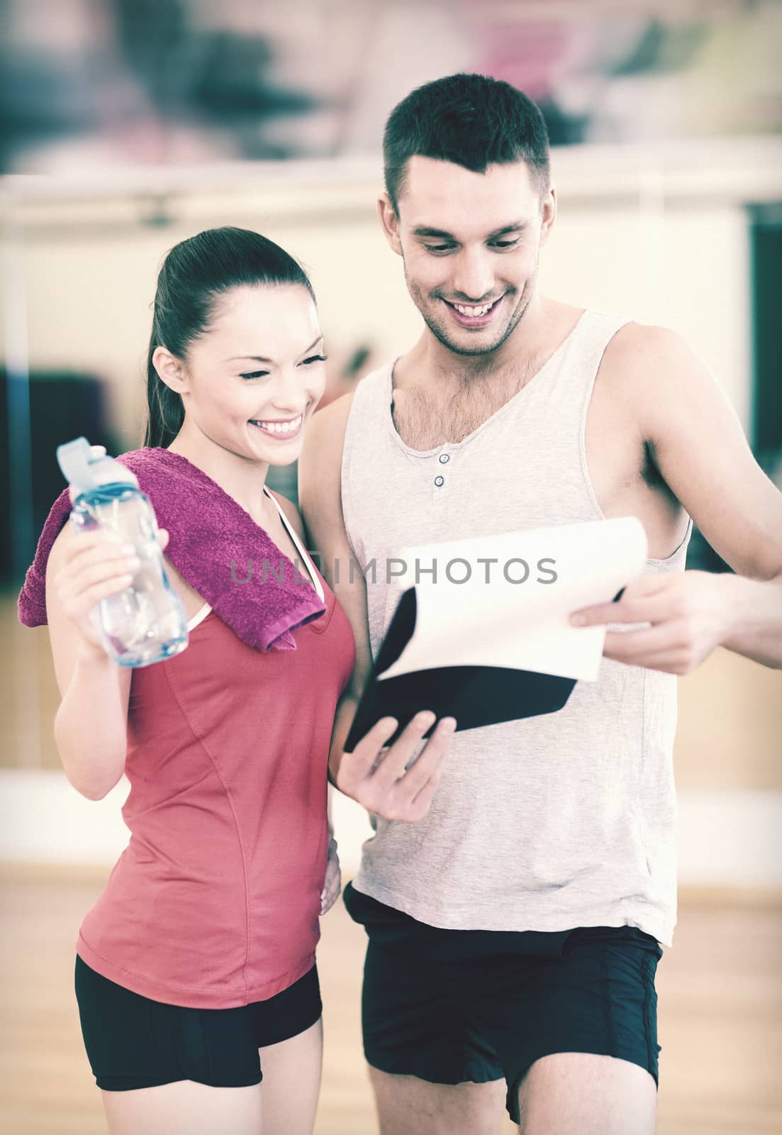 fitness, sport, training, gym and lifestyle concept - smiling male trainer with clipboard and woman with water bottle in the gym