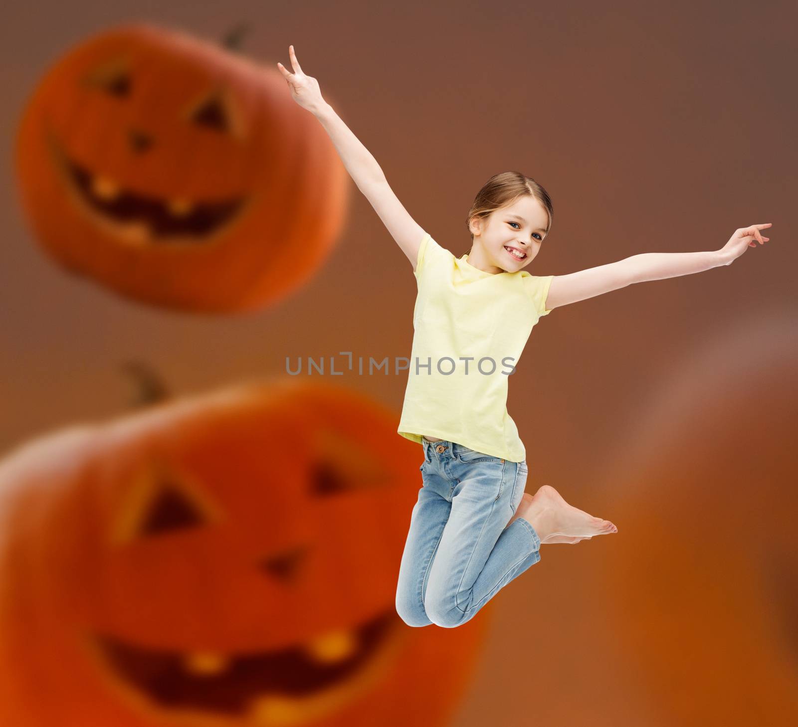 holidays, childhood, happiness and people concept - smiling little girl jumping over halloween pumpkins background