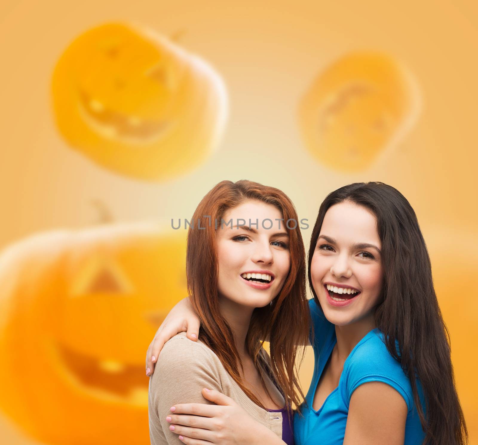 happiness, holidays, friendship and people concept - smiling teenage girls hugging over halloween pumpkins background