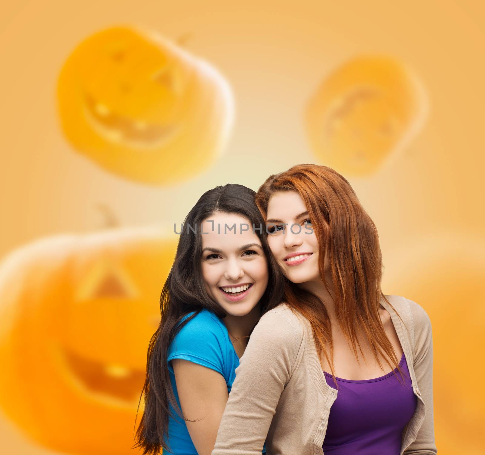 happiness, holidays, friendship and people concept - smiling teenage girls hugging over halloween pumpkins background