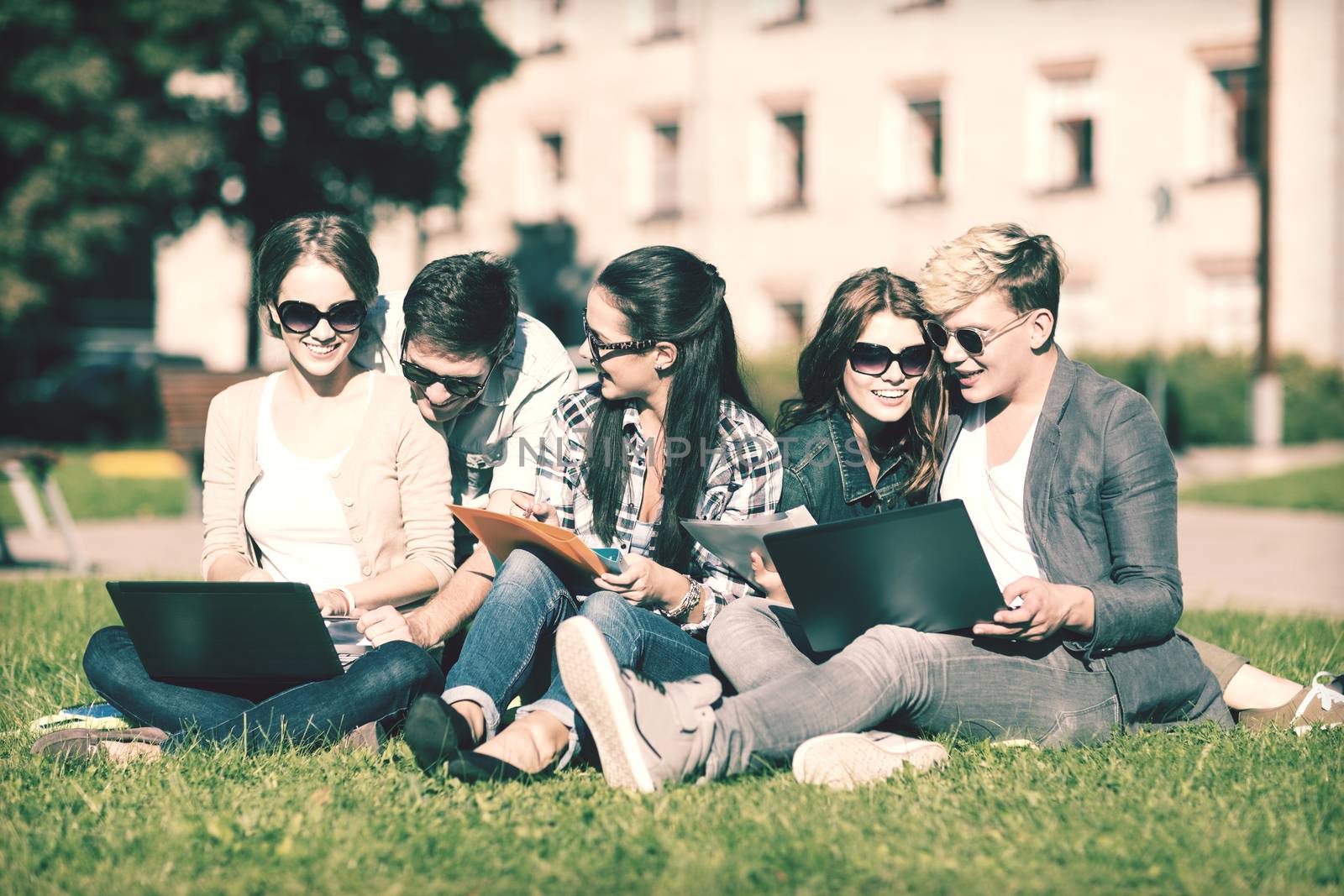 summer, internet, education, campus and teenage concept - group of students or teenagers with laptop, notebooks, files and folders