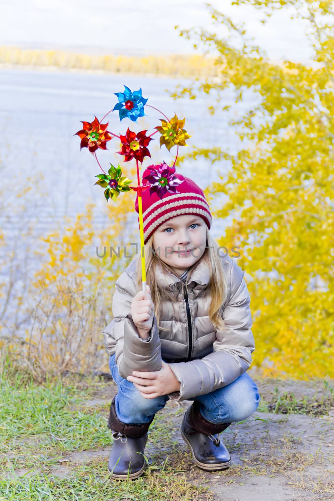 Girl with wind colorful toy on river background in autumn