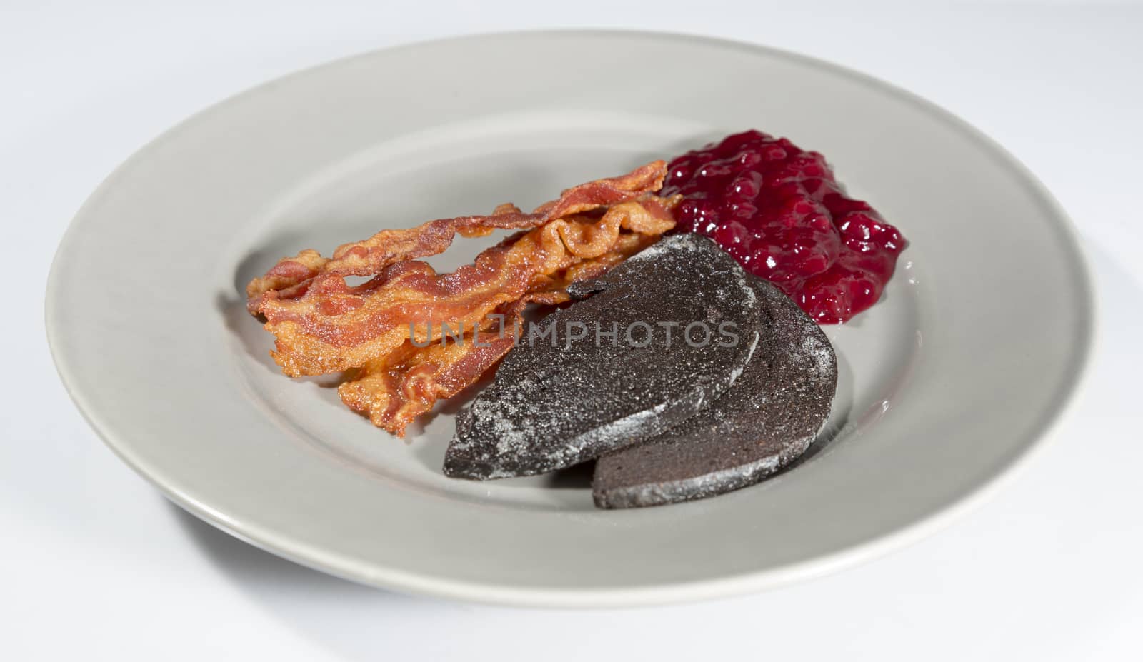Swedish Blood Pudding with Bacon and Lingonberry Jam on plate with white background.