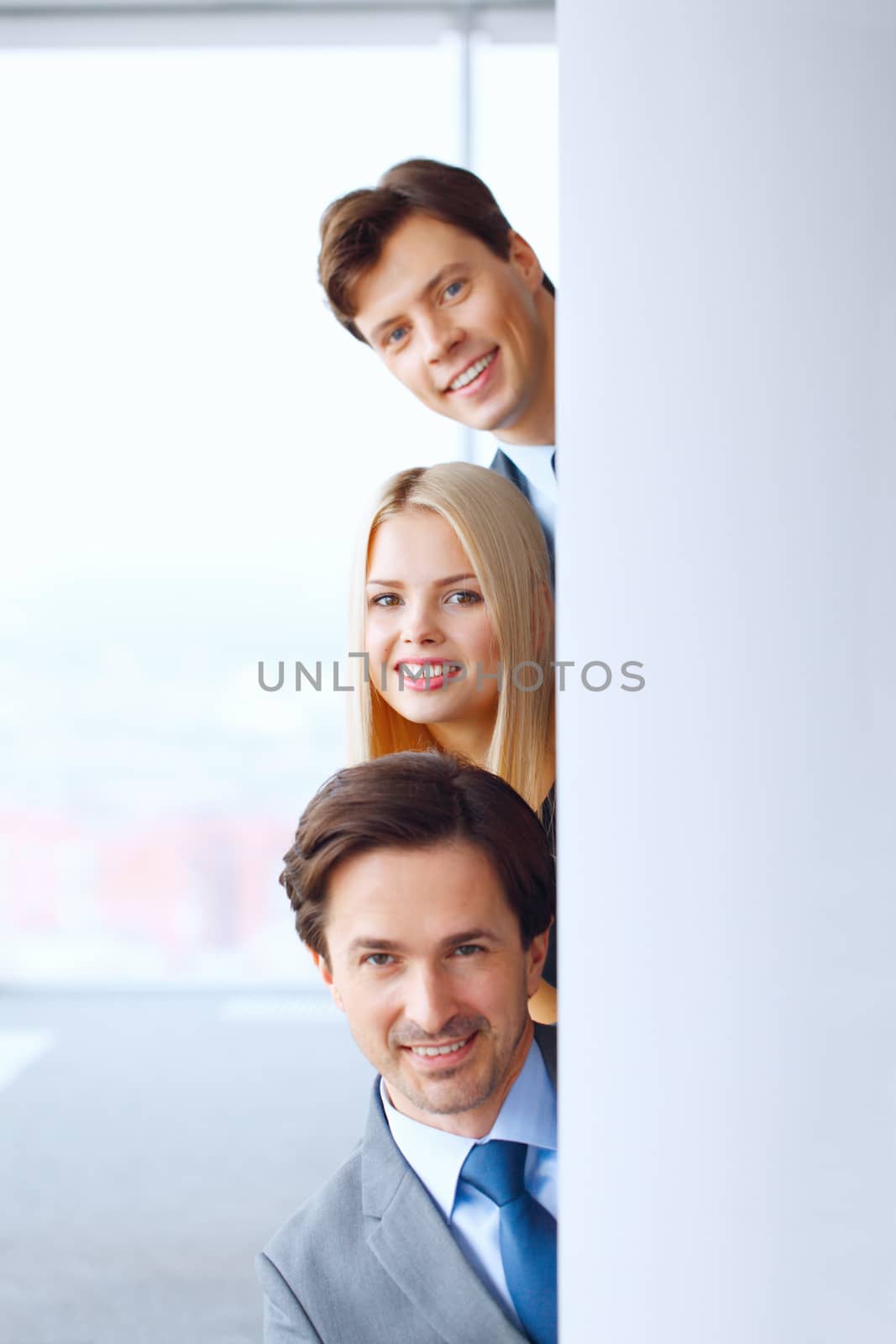 Happy business people looking out from corner in office