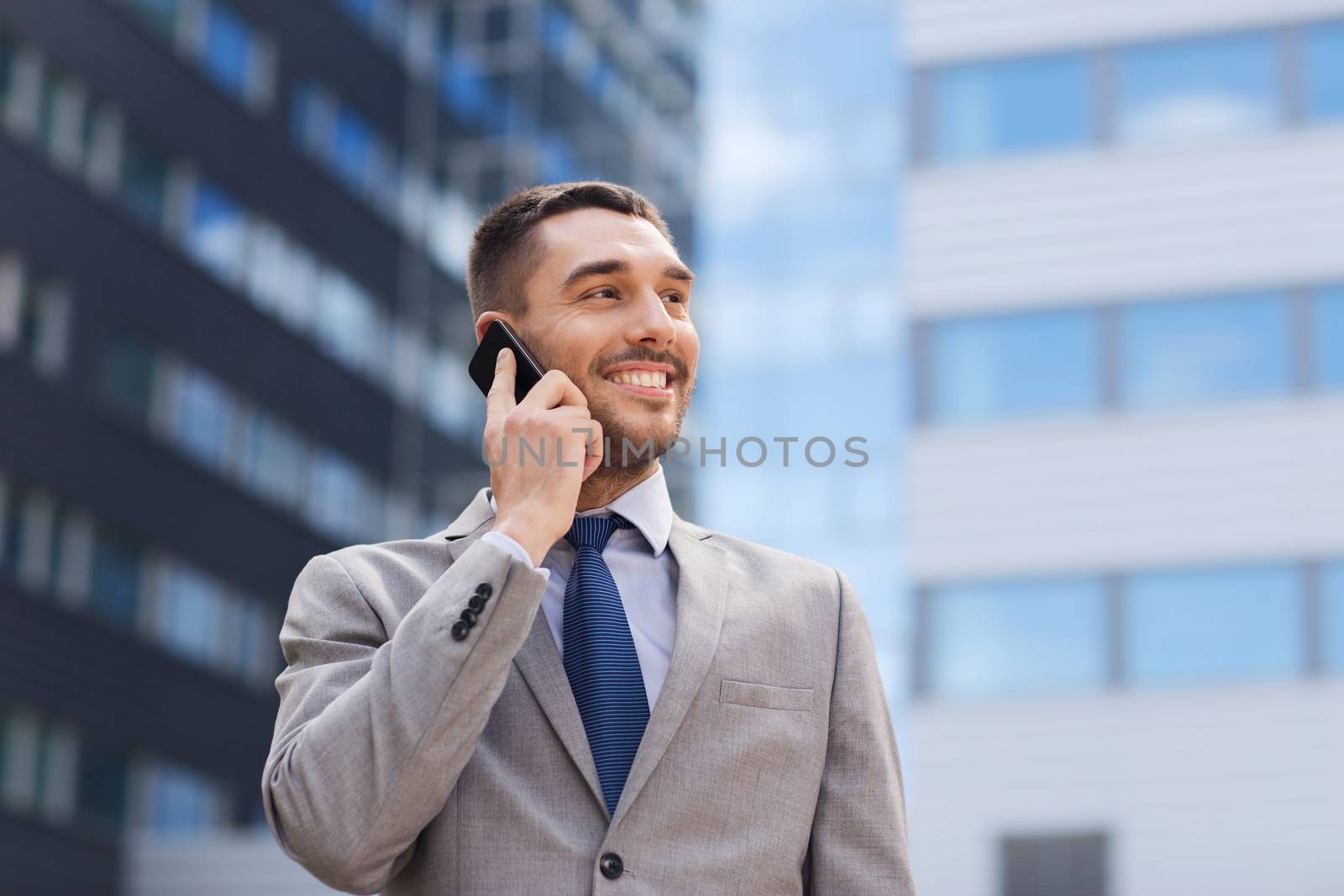 business, technology and people concept - smiling businessman with smartphone talking over office building