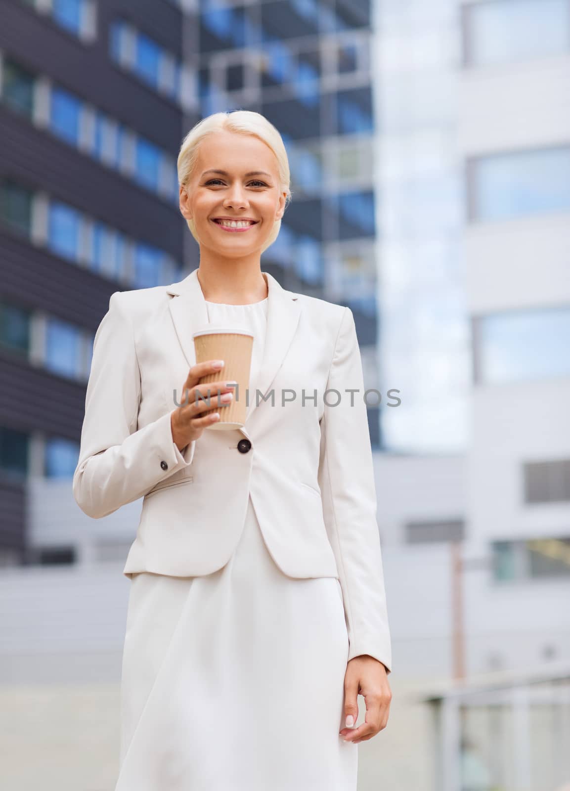 business, hot drinks and people and concept - young smiling businesswoman with paper coffee cup over office building