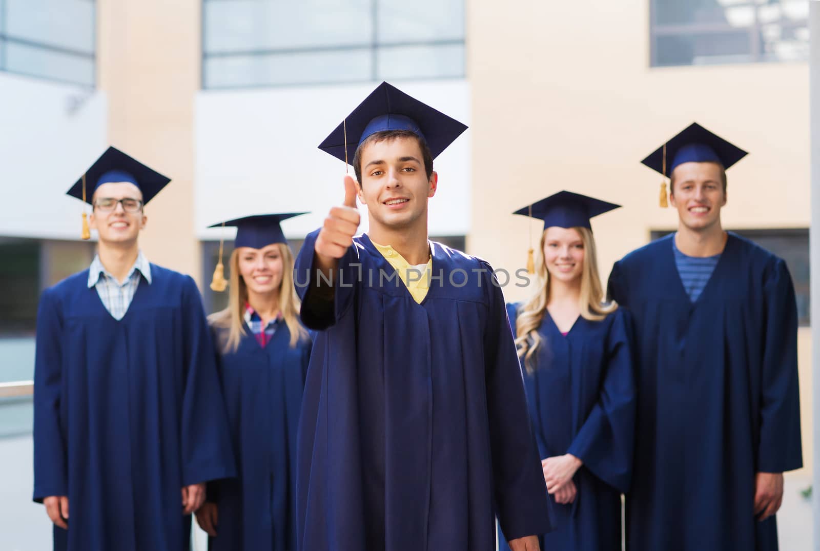 education, graduation, gesture and people concept - group of smiling students in mortarboards and gowns showing thumbs up outdoors