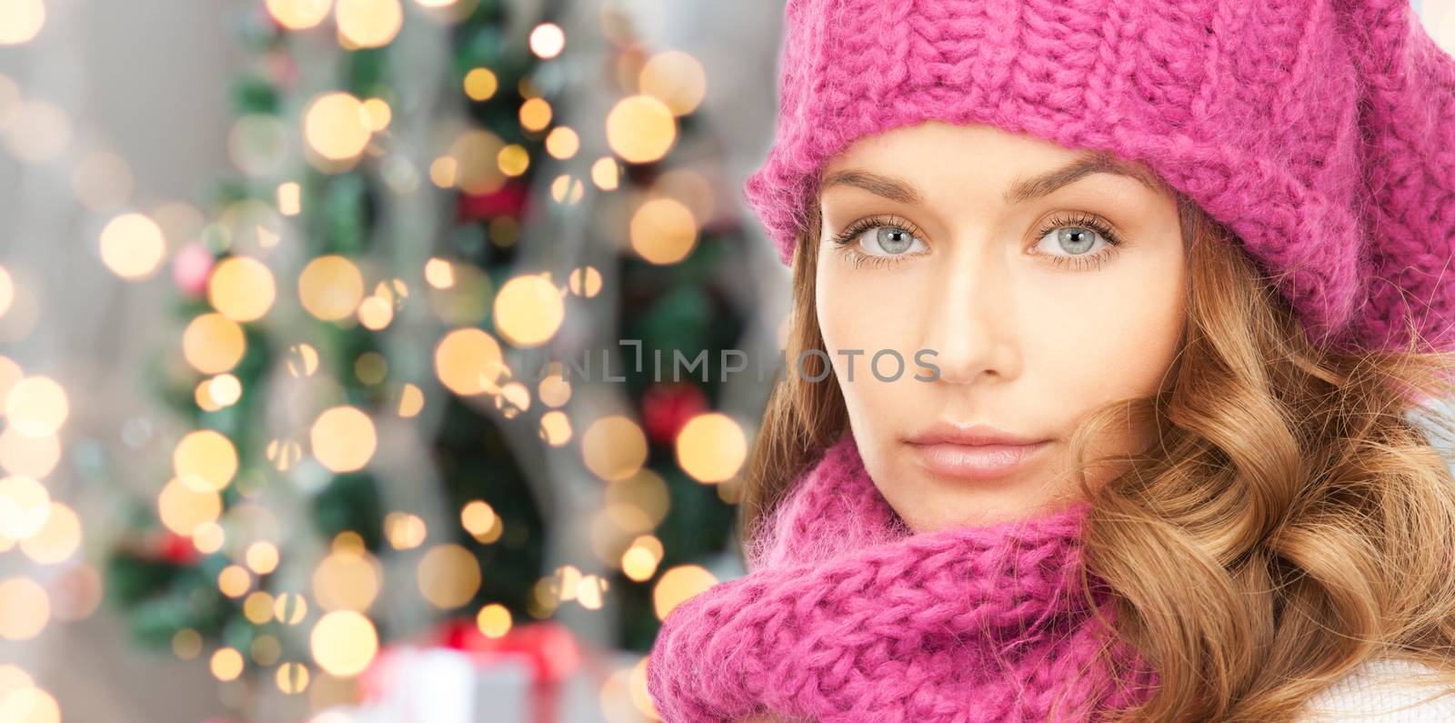 happiness, winter holidays and people concept - close up of young woman in pink hat and scarf over christmas tree lights background