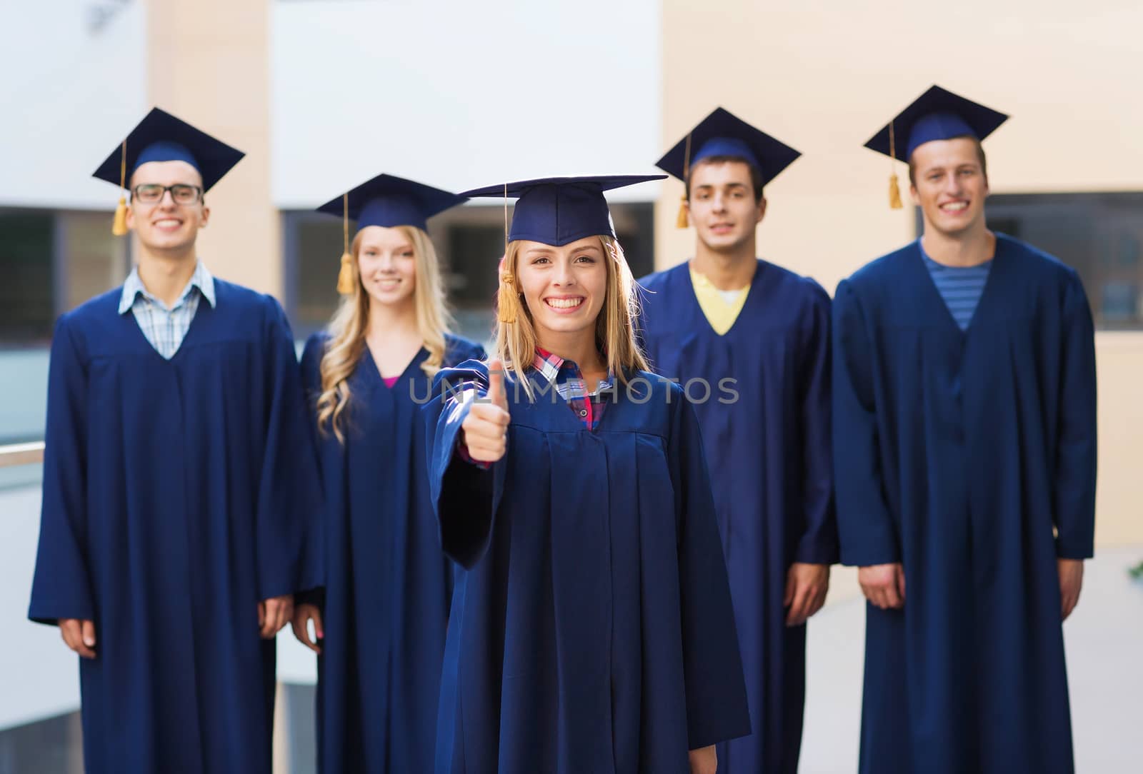 education, graduation, gesture and people concept - group of smiling students in mortarboards and gowns showing thumbs up outdoors