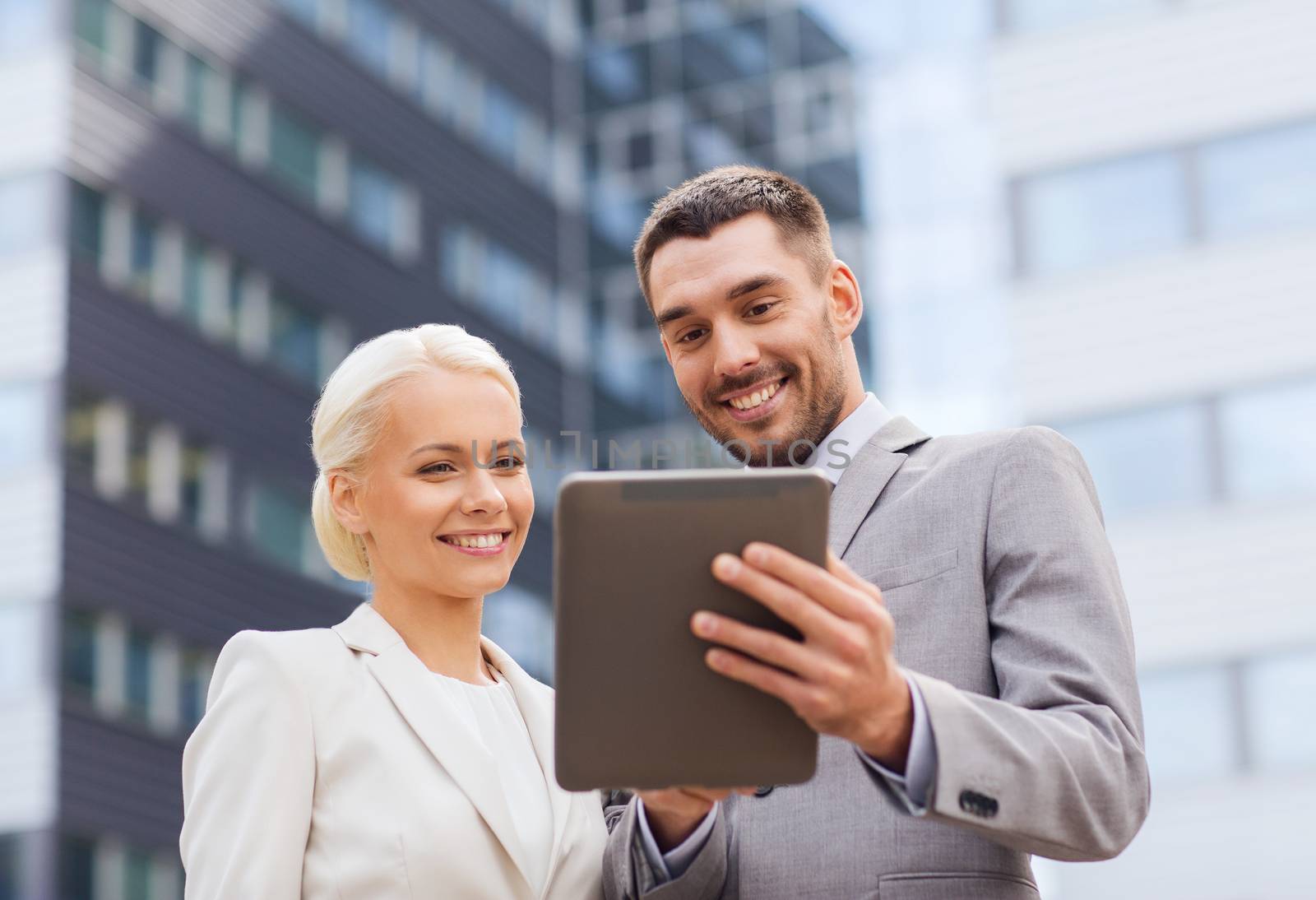 business, partnership, technology and people concept - smiling businessman and businesswoman with tablet pc computer over office building