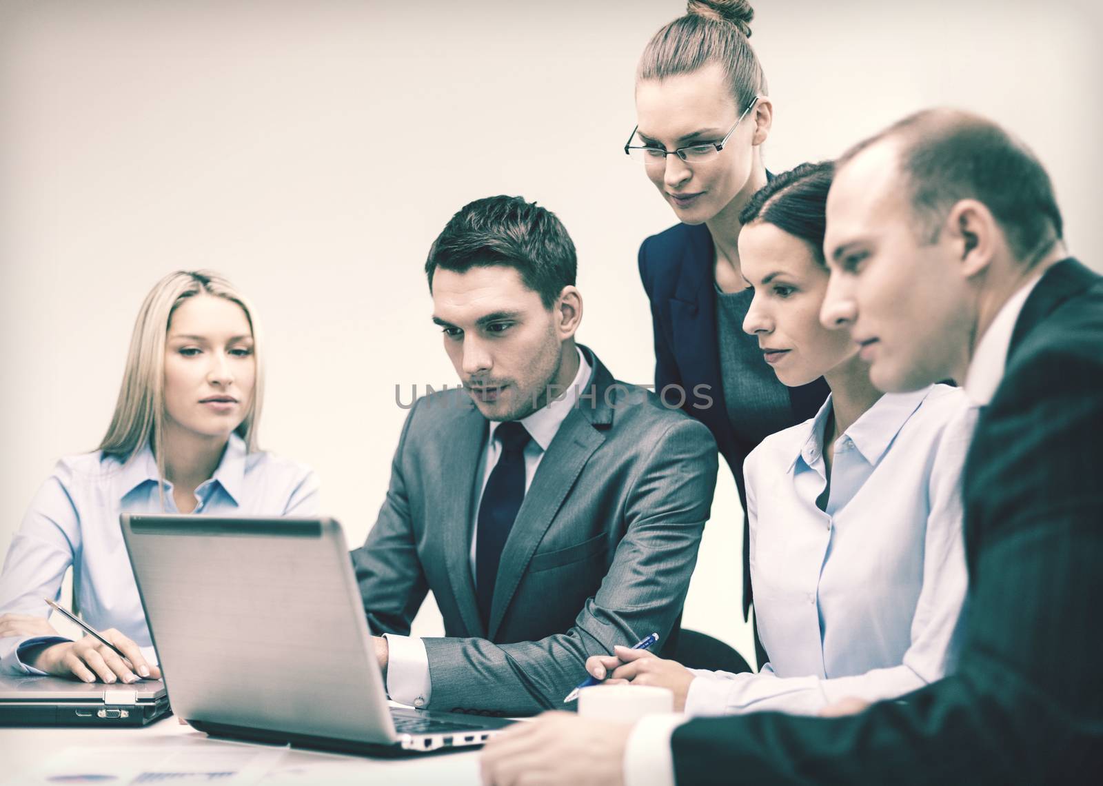 business, technology and office concept - serious business team with laptop computers, documents and coffee having discussion in office