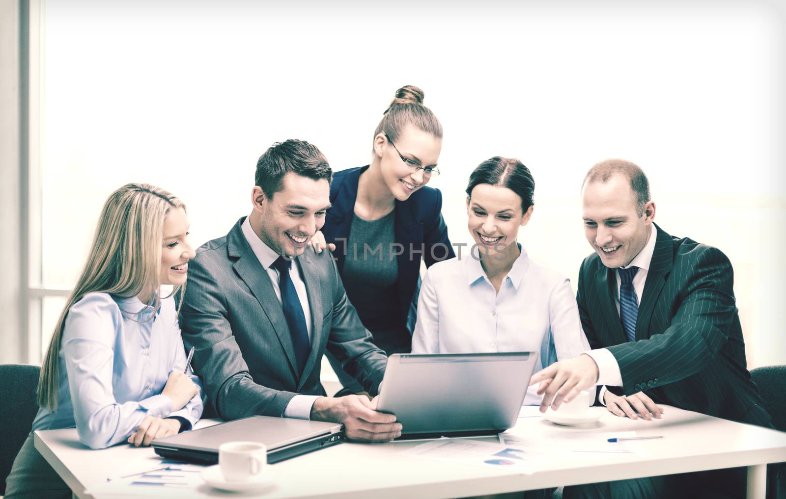 business, technology and office concept - smiling business team with laptop computers, documents and coffee having discussion in office