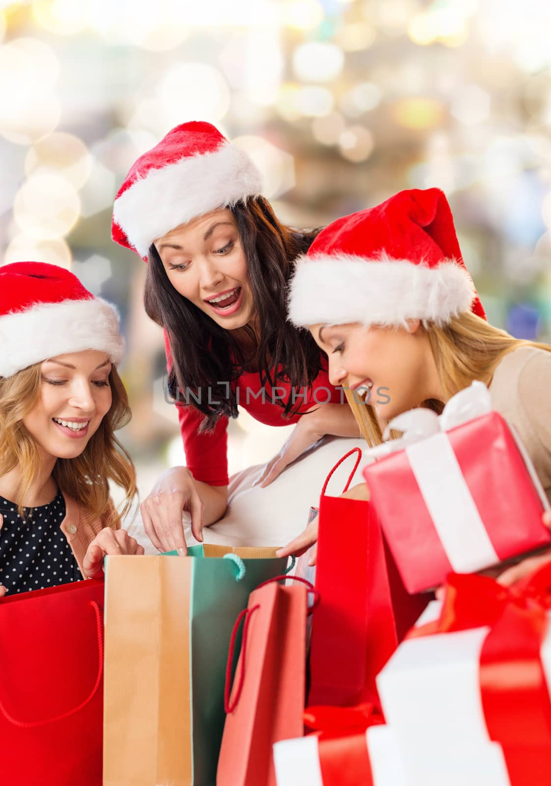 sale, winter holidays, christmas and people concept - smiling young woman in santa helper hat with gifts and shopping bags over lights background