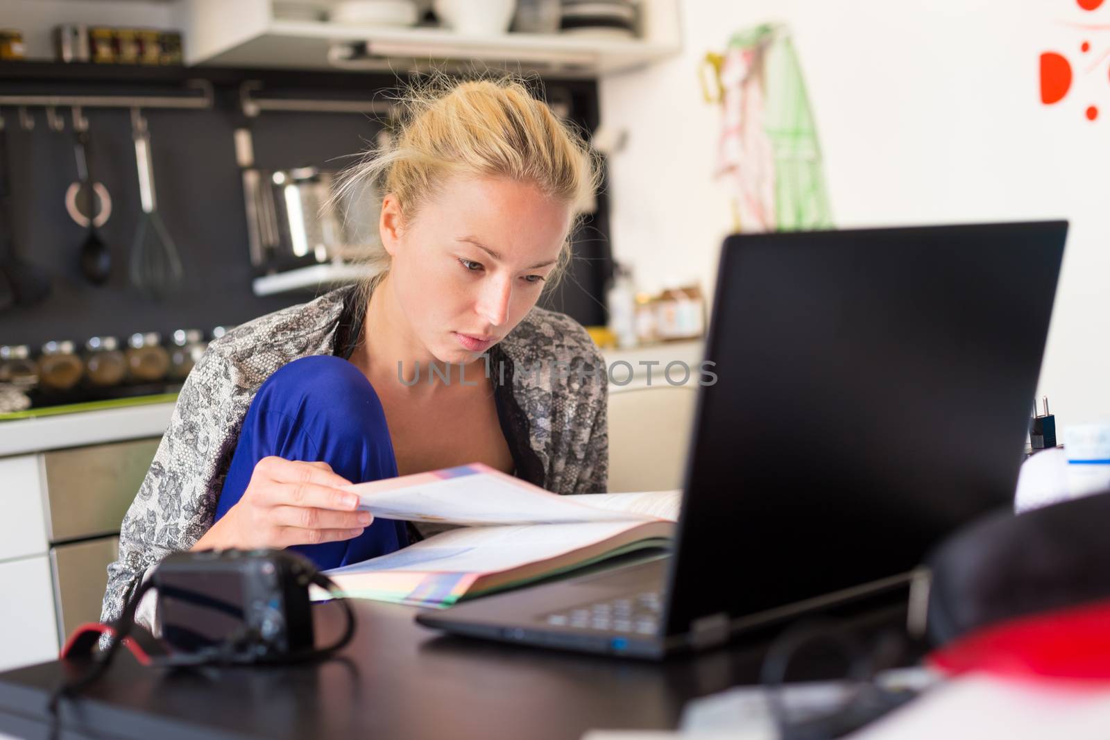 Female freelancer in her casual home clothing working remotly from her dining table in the morning. Home kitchen in the background.