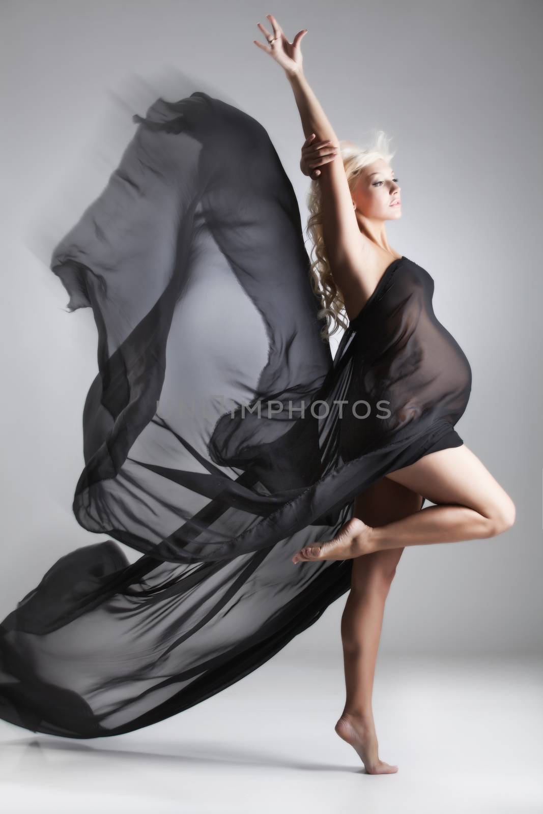 Young pregnant woman with a piece of white fabric in a motion on a studio background