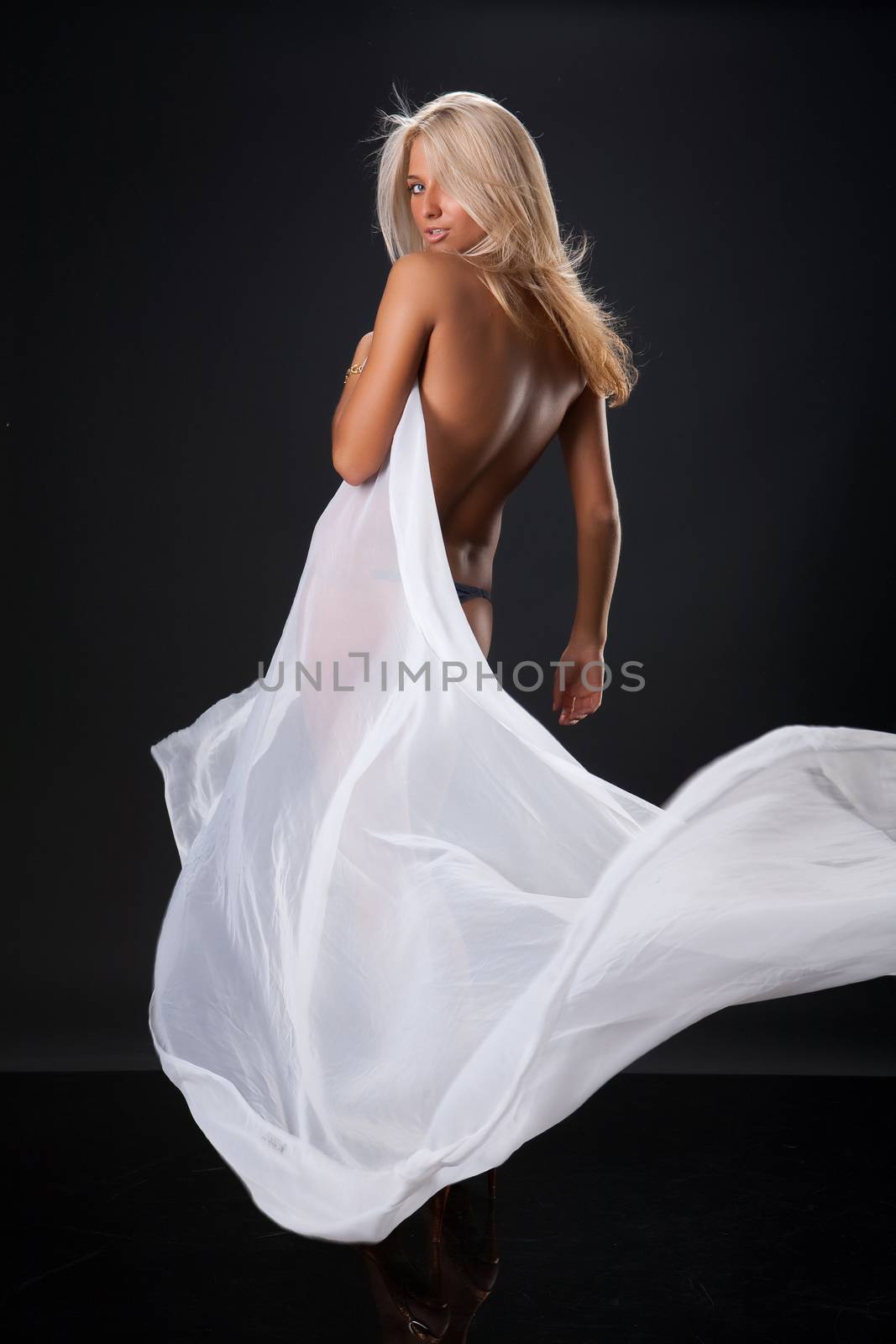 Young topless blonde woman with a waving white fabric on black reflecting background