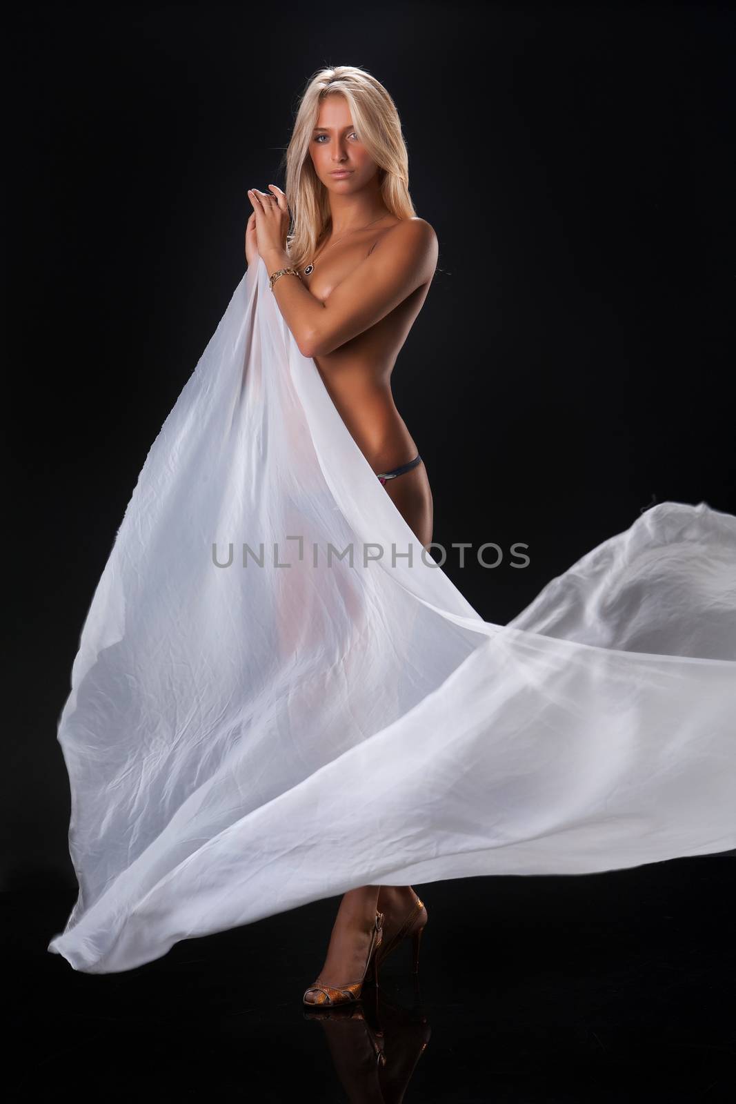 Young topless blonde woman with a waving white fabric on black reflecting background