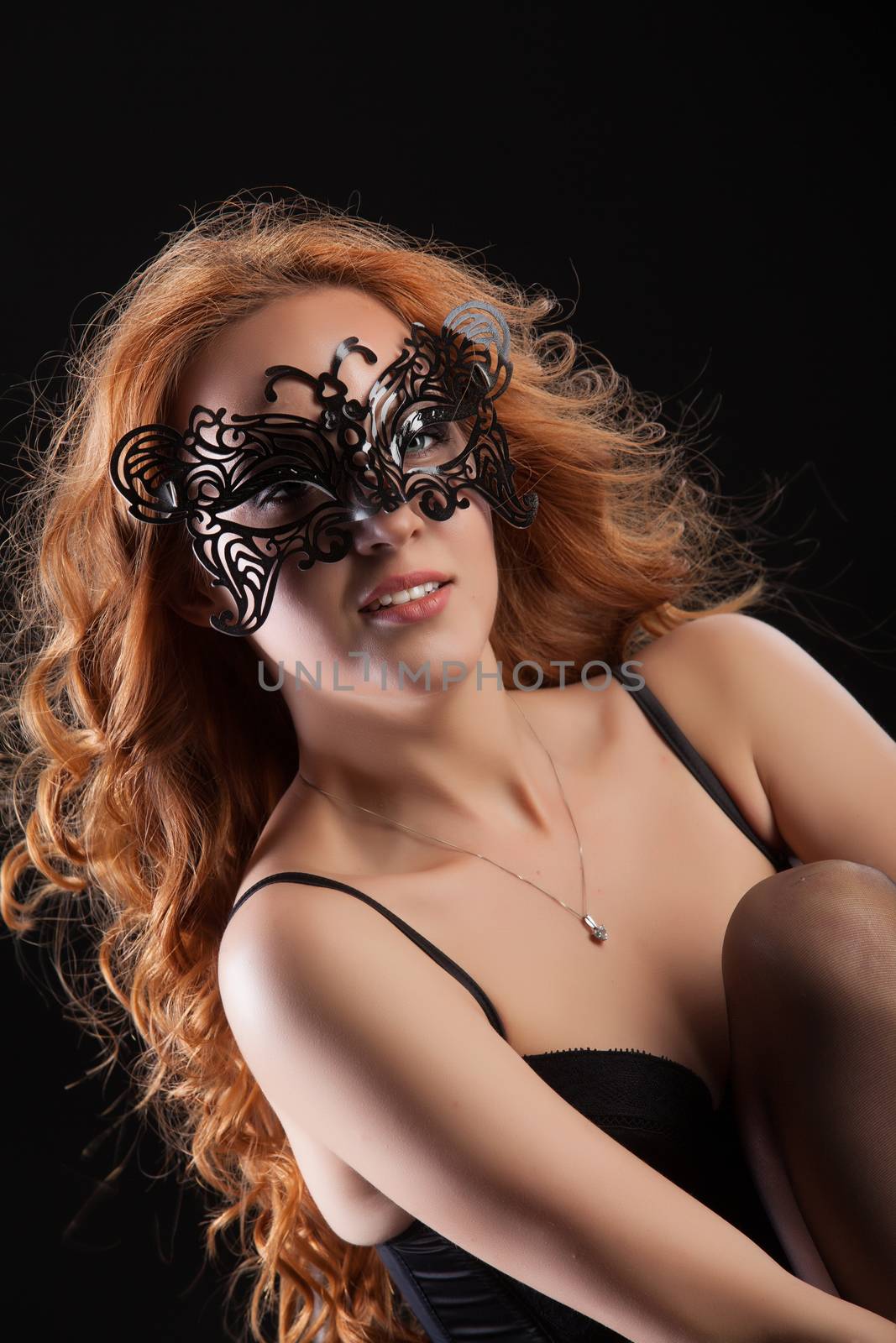 Young red- haired woman in a black lingerie on a studio background