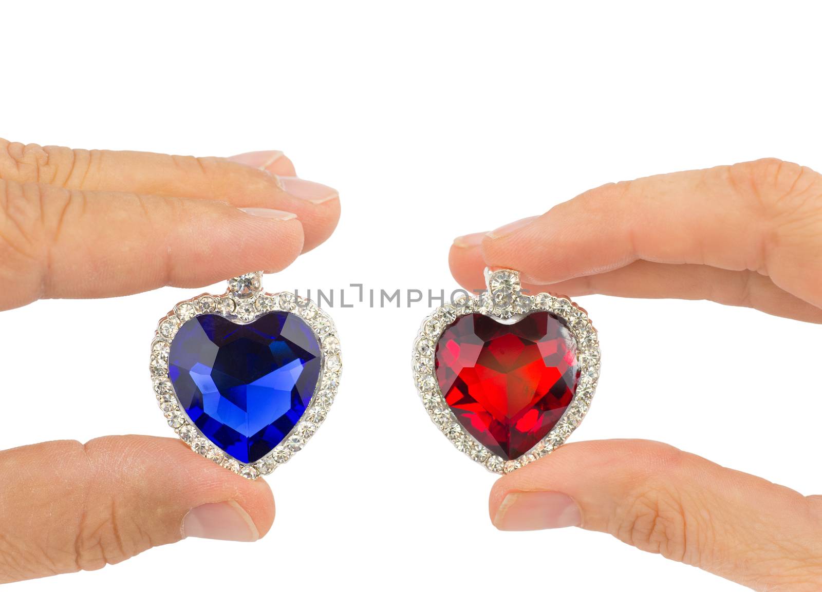 Fingers of man and woman holding blue and red jewelry hearts isolated on white background