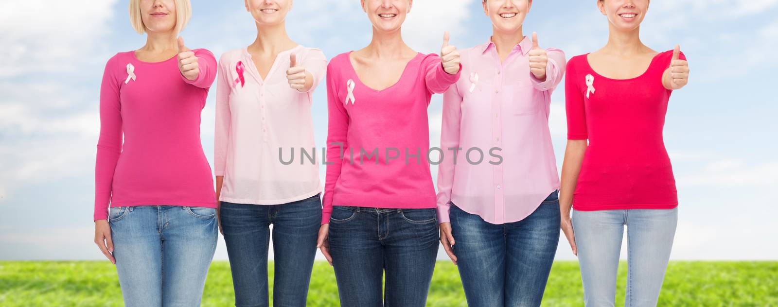 healthcare, people, gesture and medicine concept - close up of smiling women in blank shirts with pink breast cancer awareness ribbons over blue sky and grass background