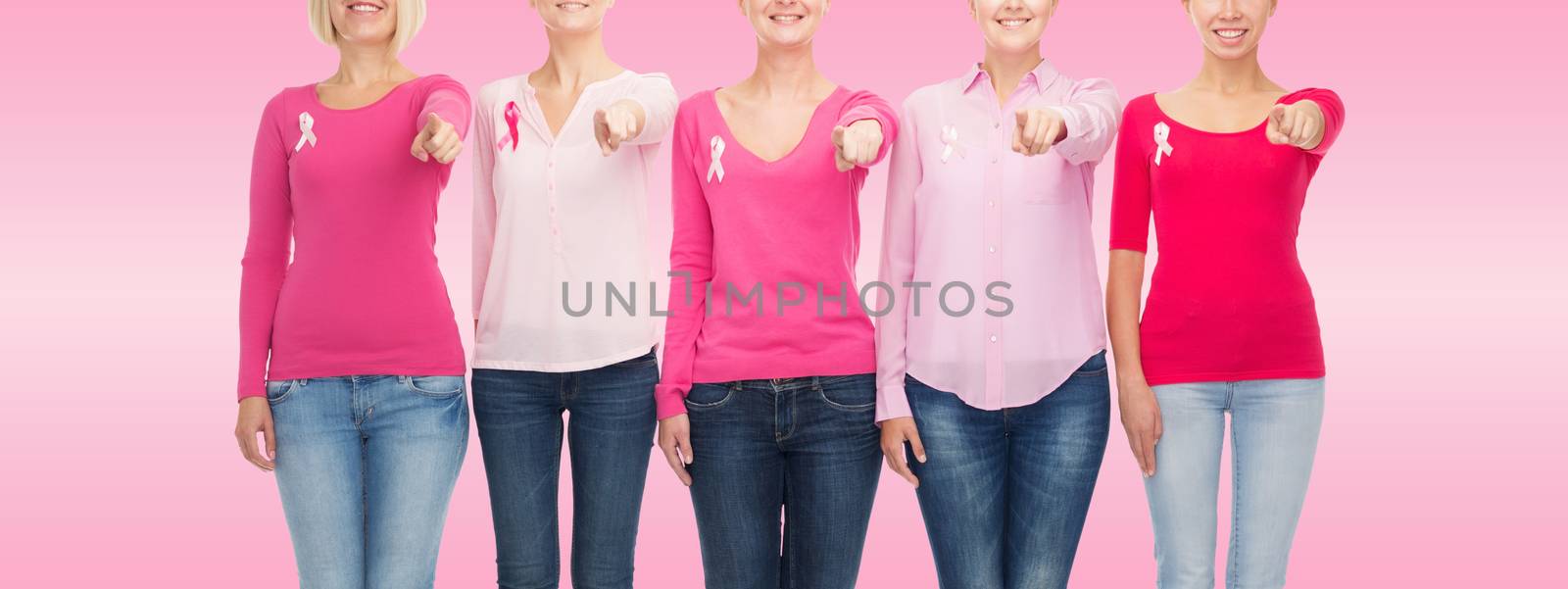 healthcare, people, gesture and medicine concept - close up of smiling women in blank shirts with breast cancer awareness ribbons pointing on you over pink background