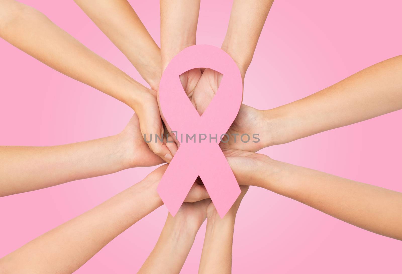 healthcare, people and medicine concept - close up of women hands with paper cancer awareness symbol over pink background