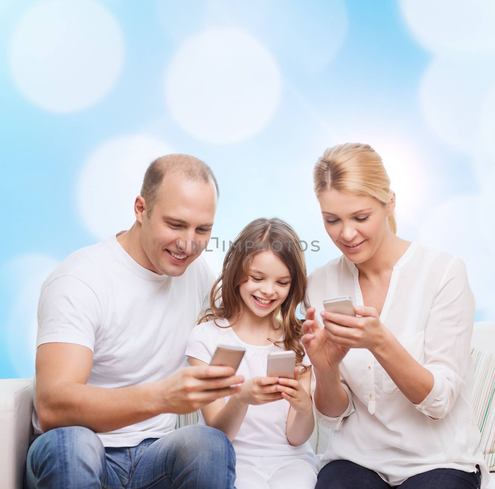 family, holidays, technology and people concept - smiling mother, father and little girl with smartphones over blue lights background