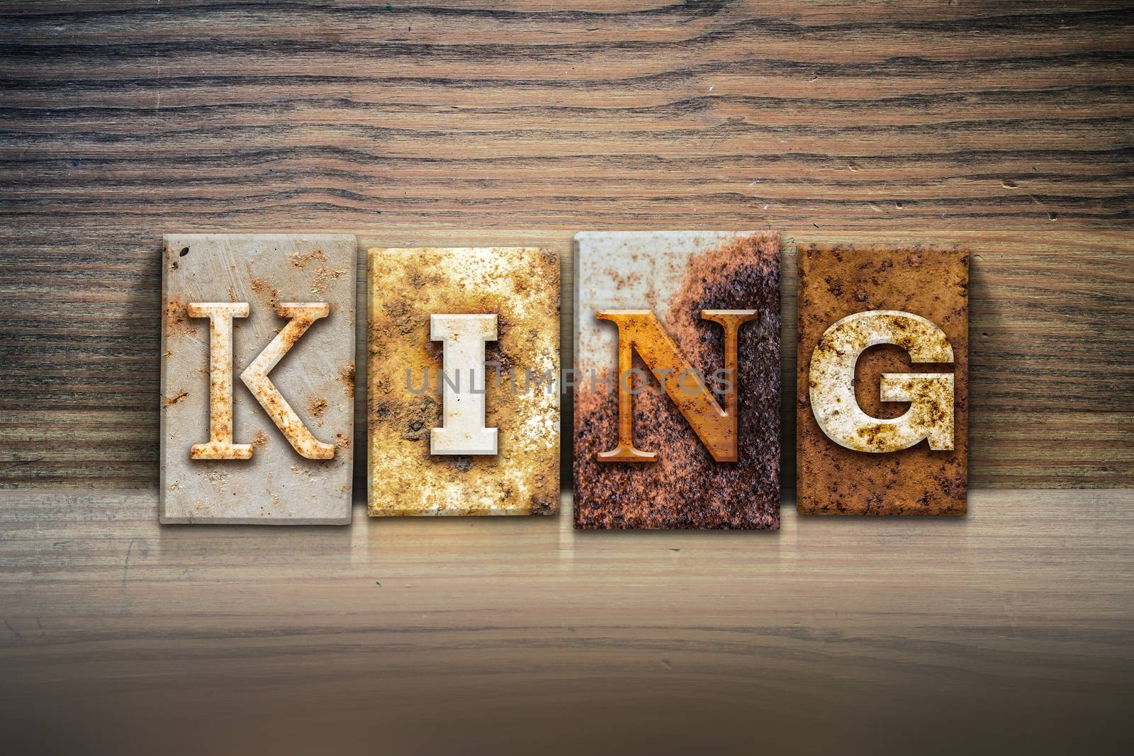 The word "KING" written in rusty metal letterpress type sitting on a wooden ledge background.