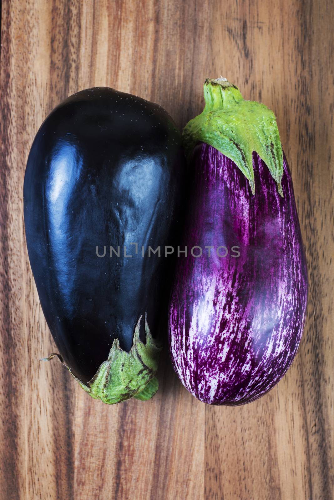 Fresh ripe aubergine and stripped raw eggplants over wood background