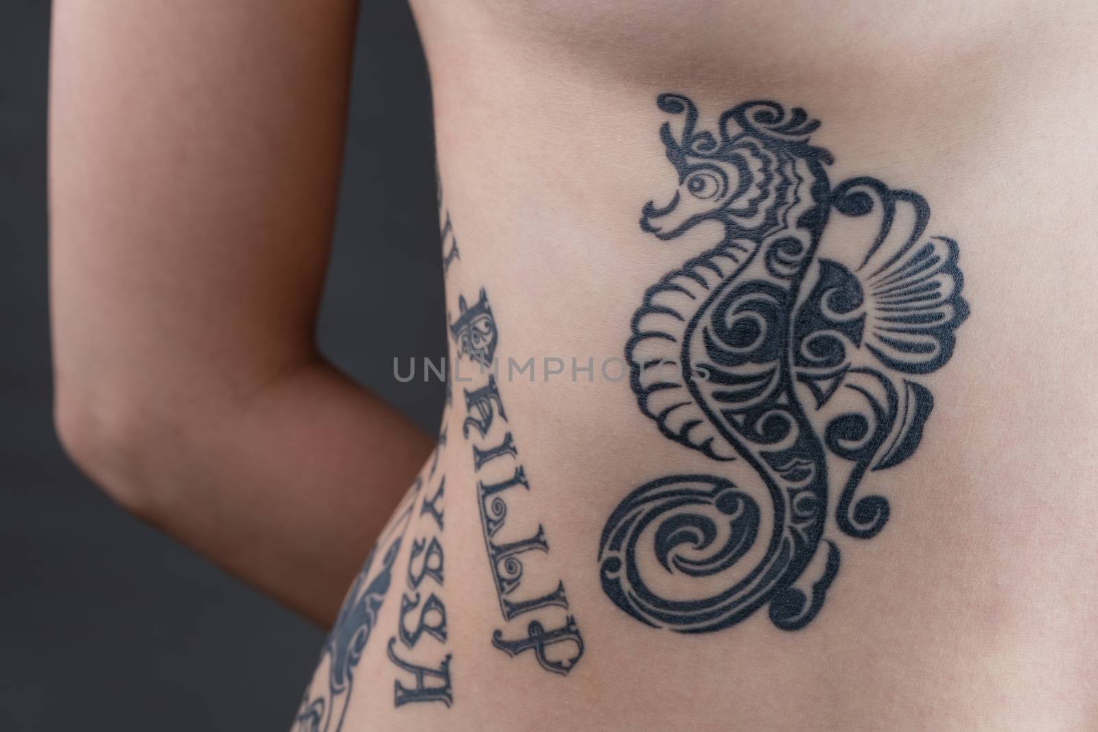 A tattoo of a black tribal style seahorse with children's names wrapping around a woman's ribs.