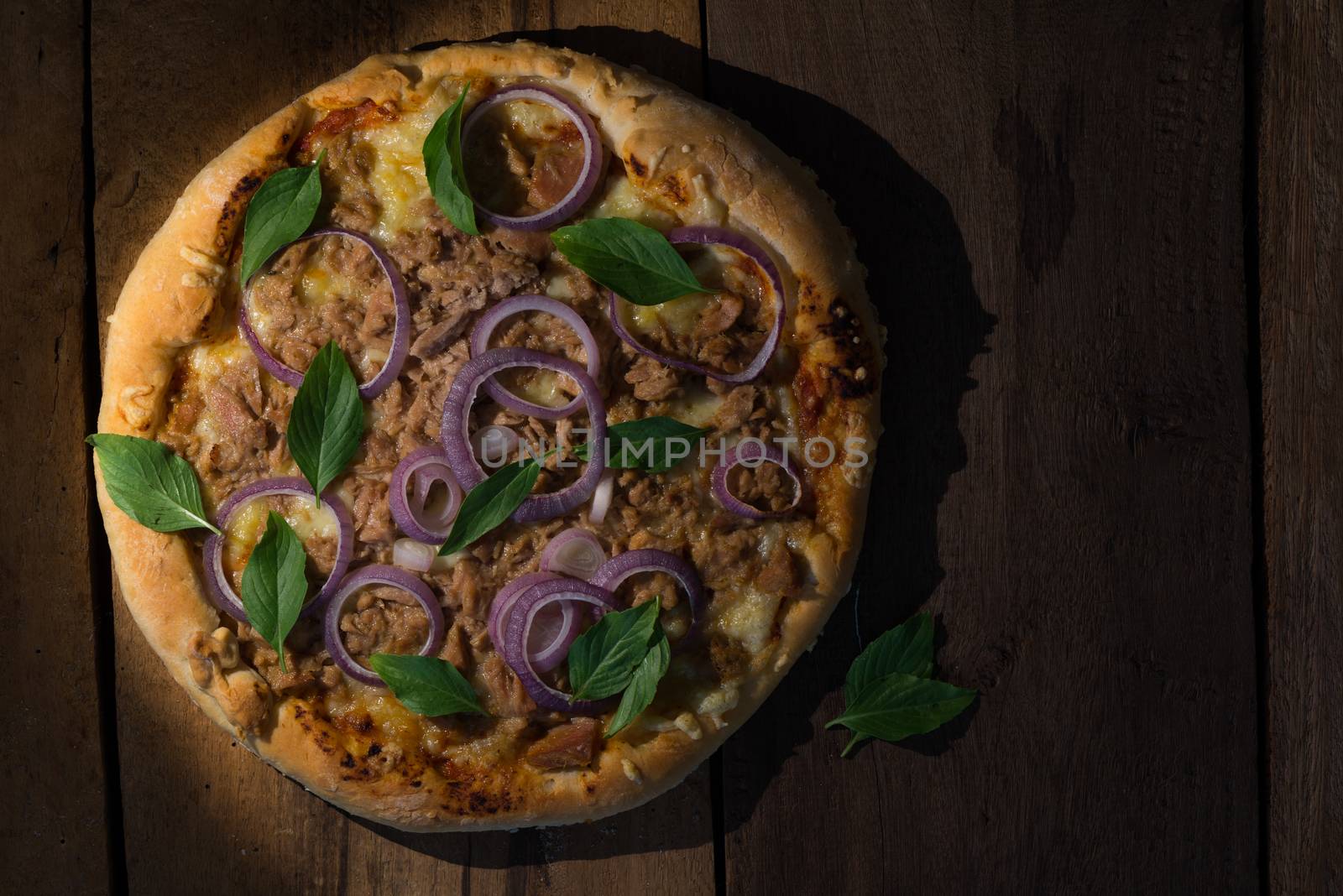 top view of a round tuna pizza with onion rings on a dark wooden table