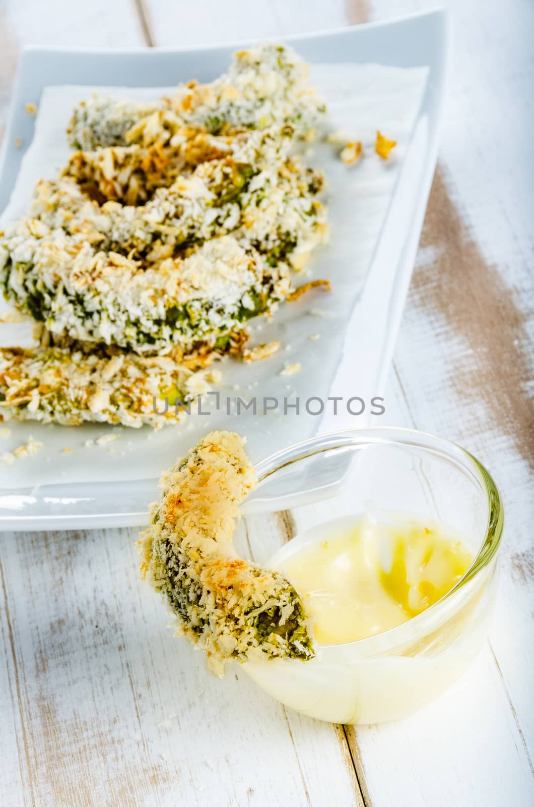breaded baked avocado pieces served with a mayonnaise sauce on porcelain plate and white wood background