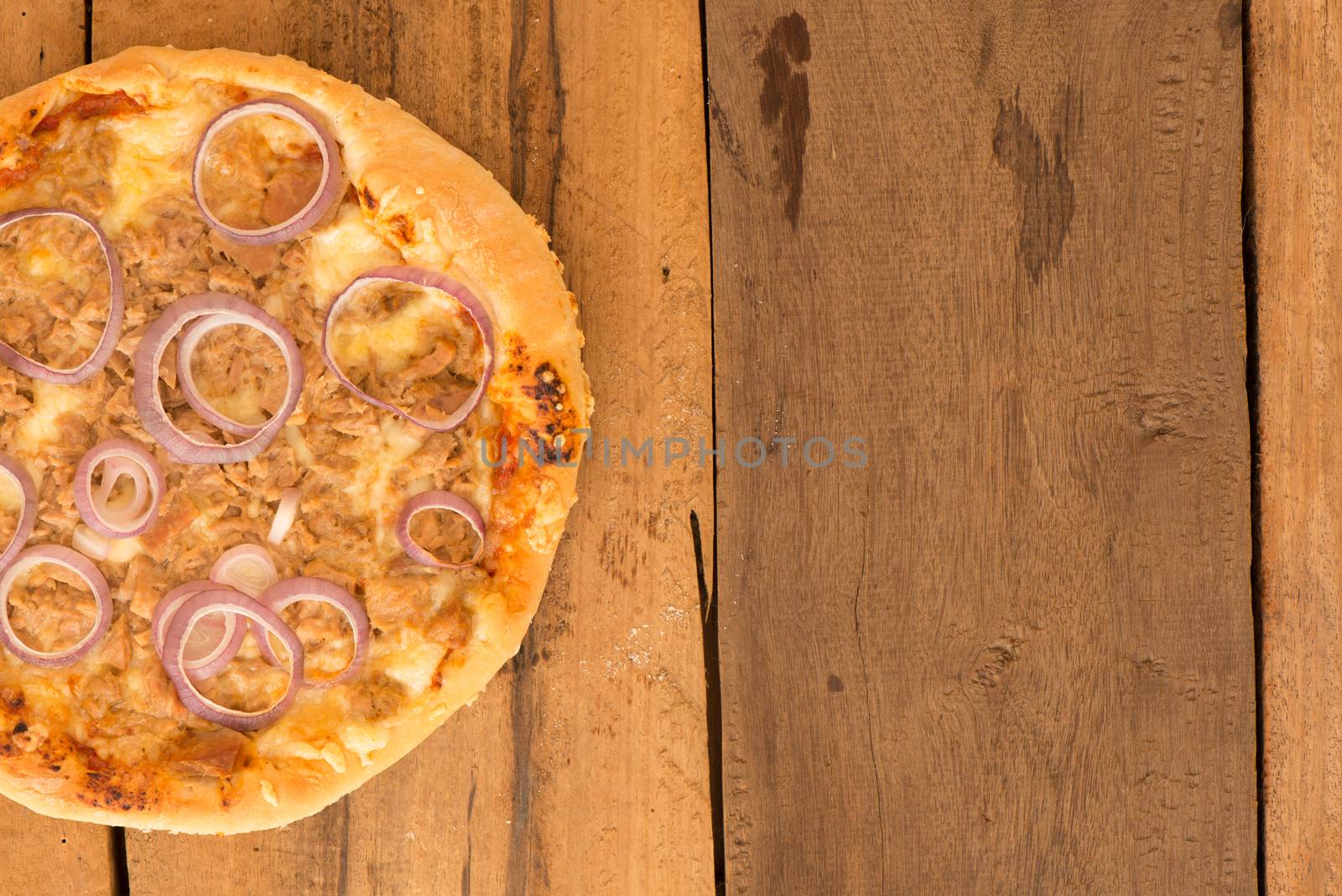 top view a round tuna pizza with onion rings on a wooden table