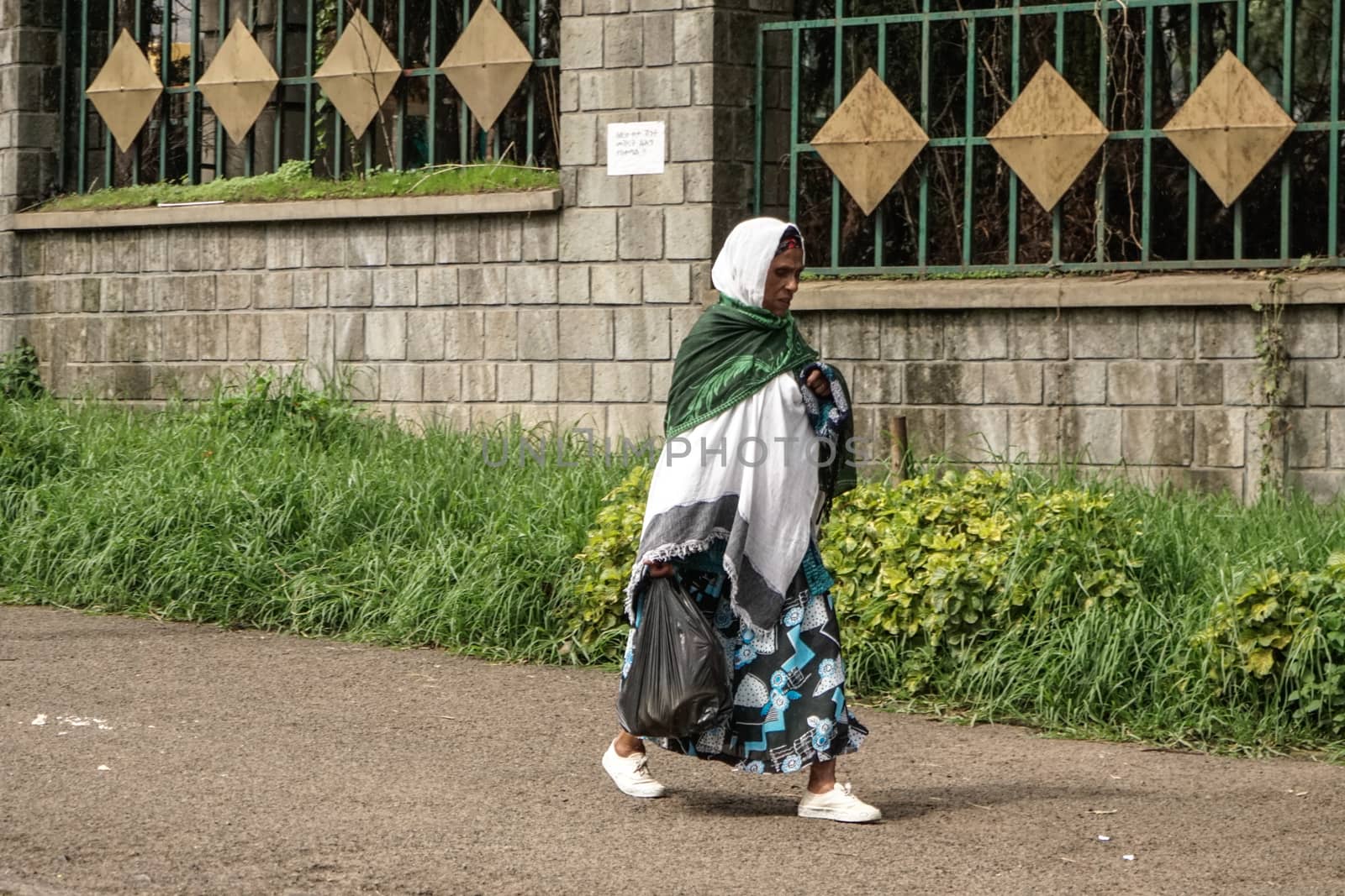 Addis Ababa - July 26: An older woman wearing a mix of modern and traditional clothing returns from the market carrying her groceries in a plastic bag on June 26, 2015 in Addis Ababa, Ethiopia.