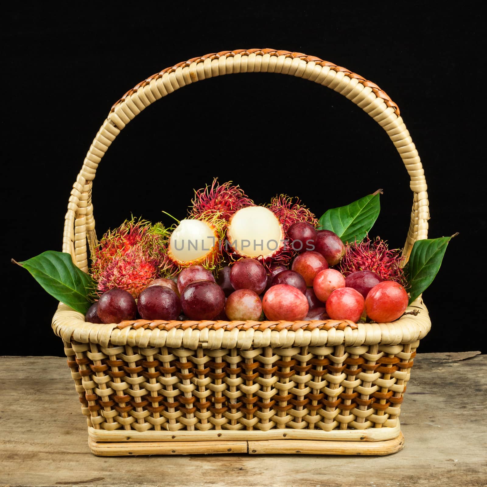 fresh fruit red grapes and rambutan in basket on wood background by nopparats