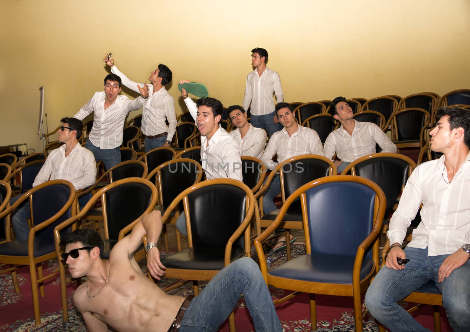 Multiple postures of a handsome young man in a hall or auditorium sitting in various positions in comfortable armchairs, standing and lounging shirtless on the floor