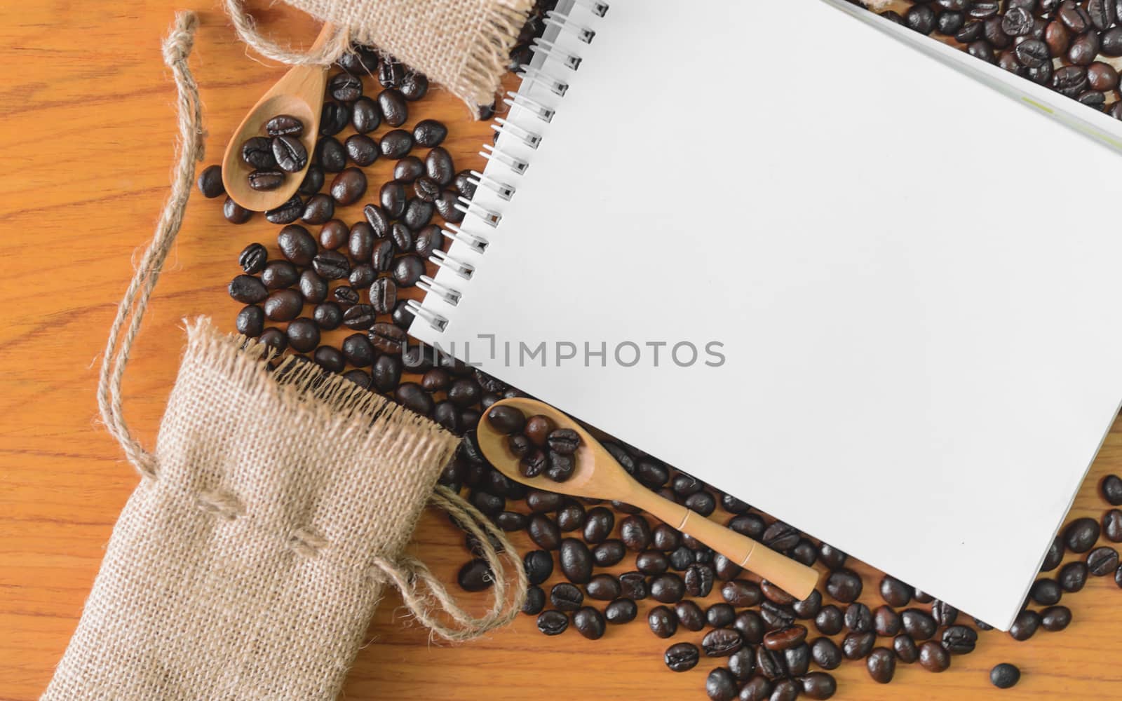 White notebook for your text with sackcloth and coffee beans on wooden spoon.