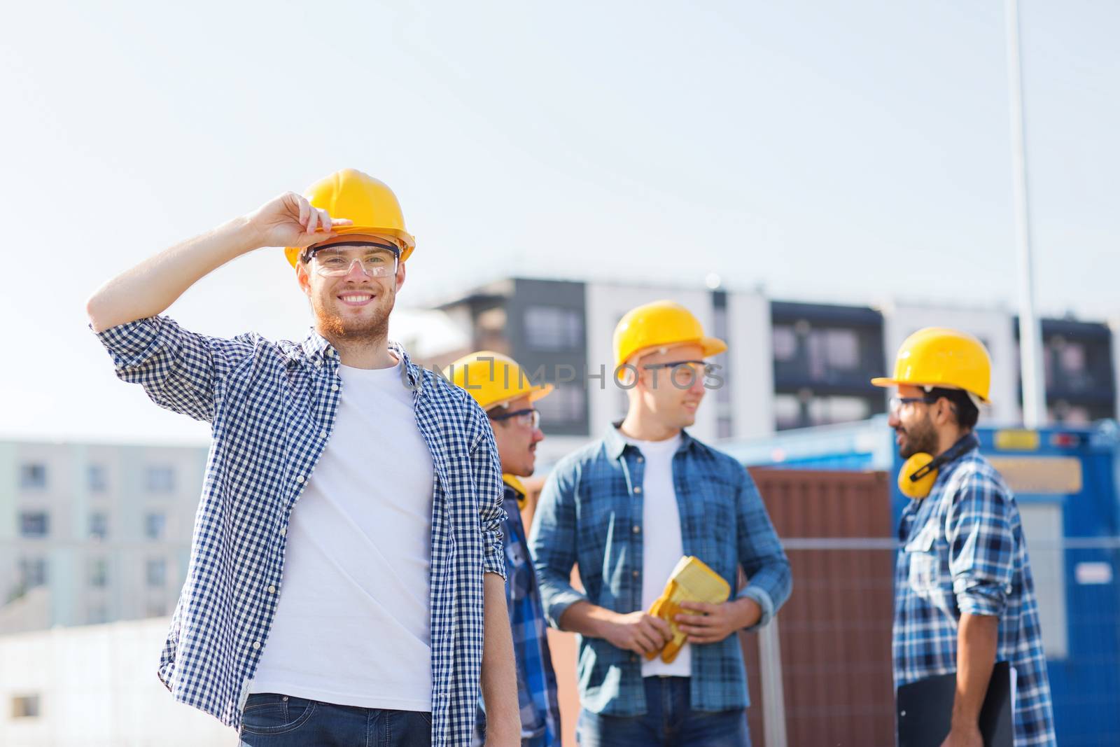 group of smiling builders in hardhats outdoors by dolgachov