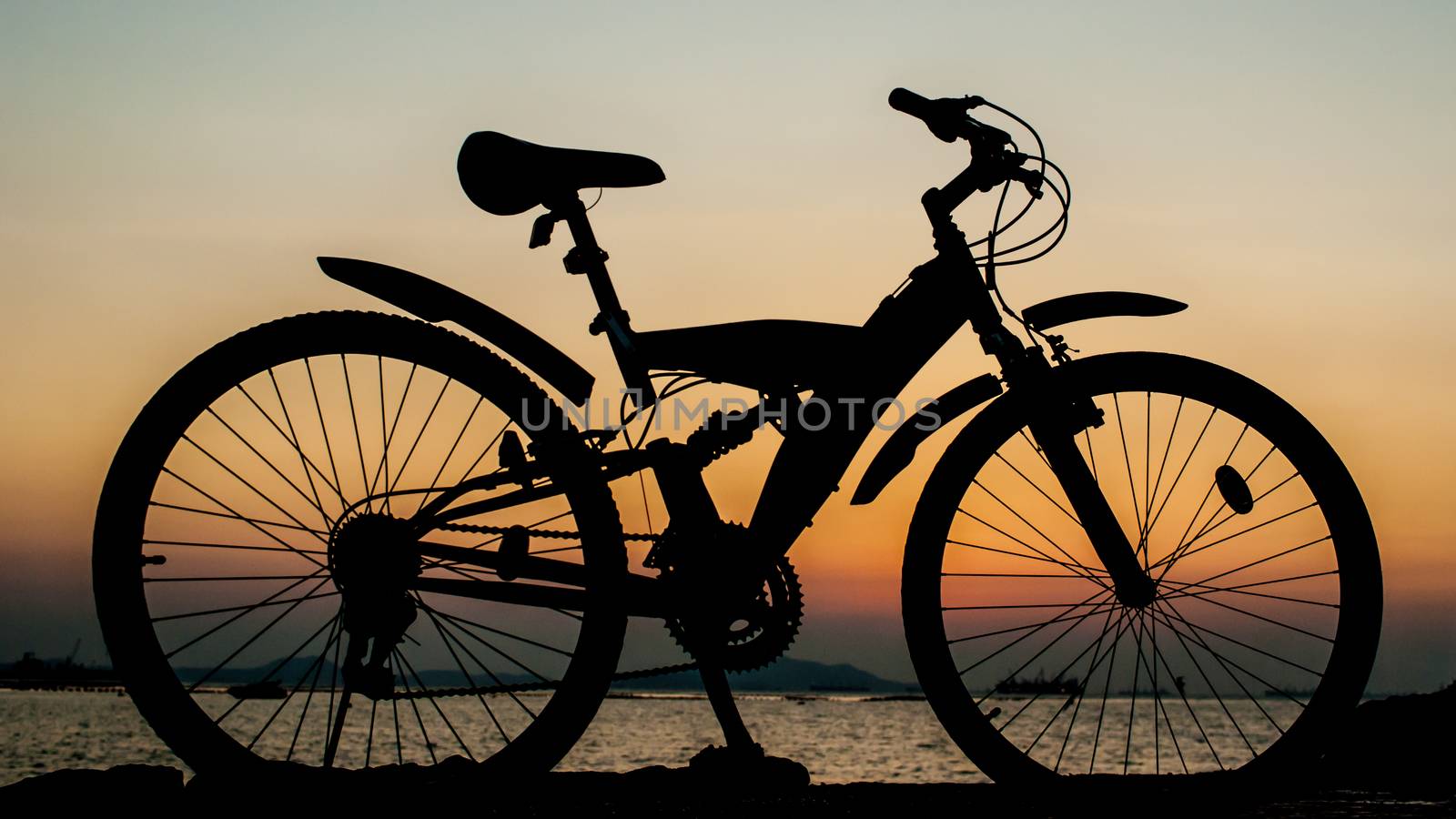 Silhouette of mountain bike parking on jetty beside sea with sunset sky background