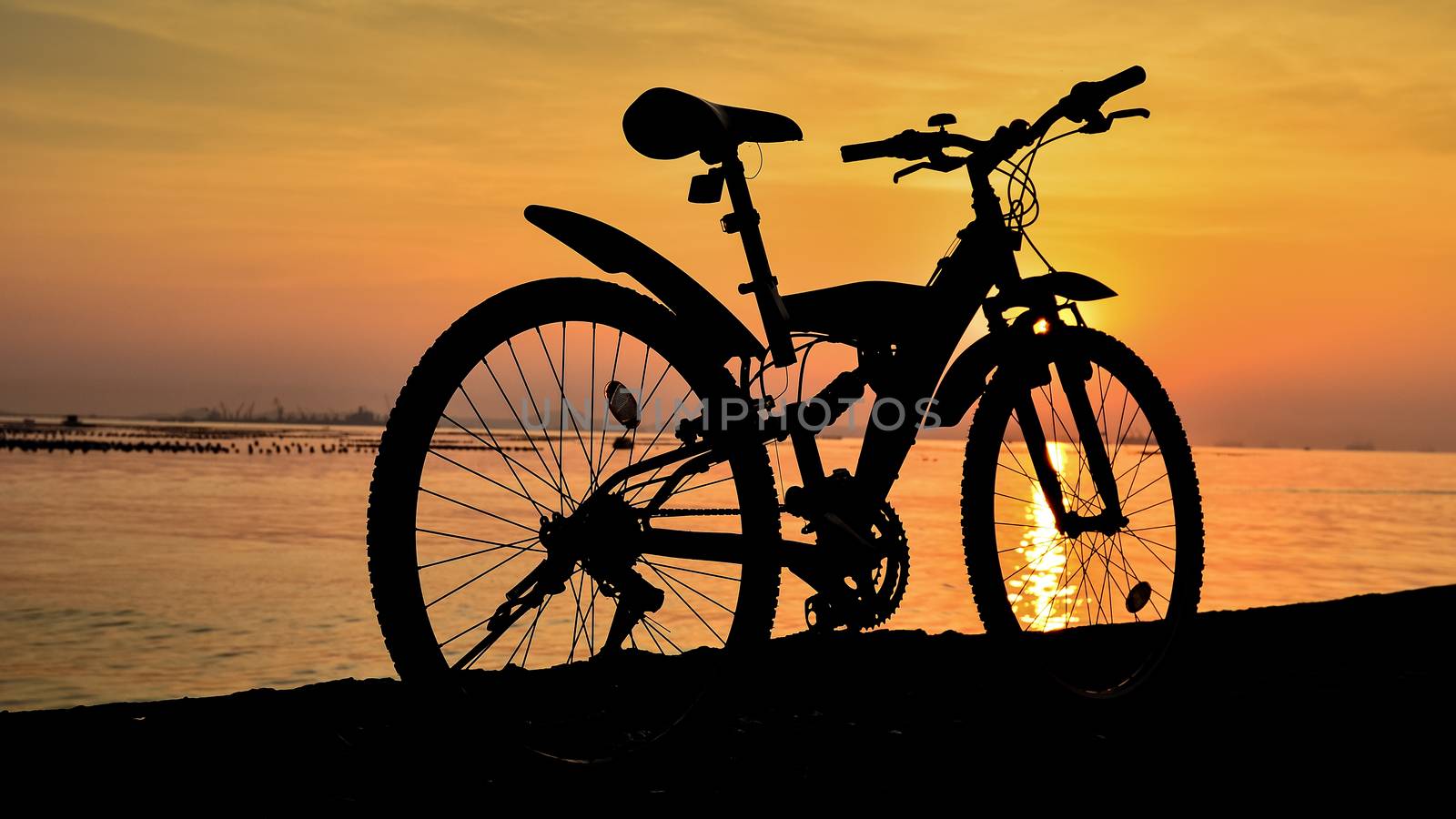 Silhouette of mountain bike parking on jetty beside sea with sunset sky background