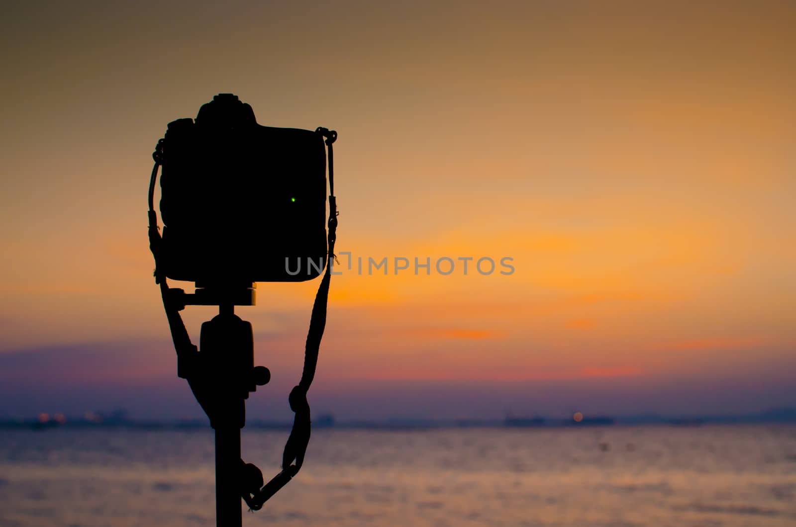 Silhouette of DSLR camera at sea with sunset sky by pixbox77