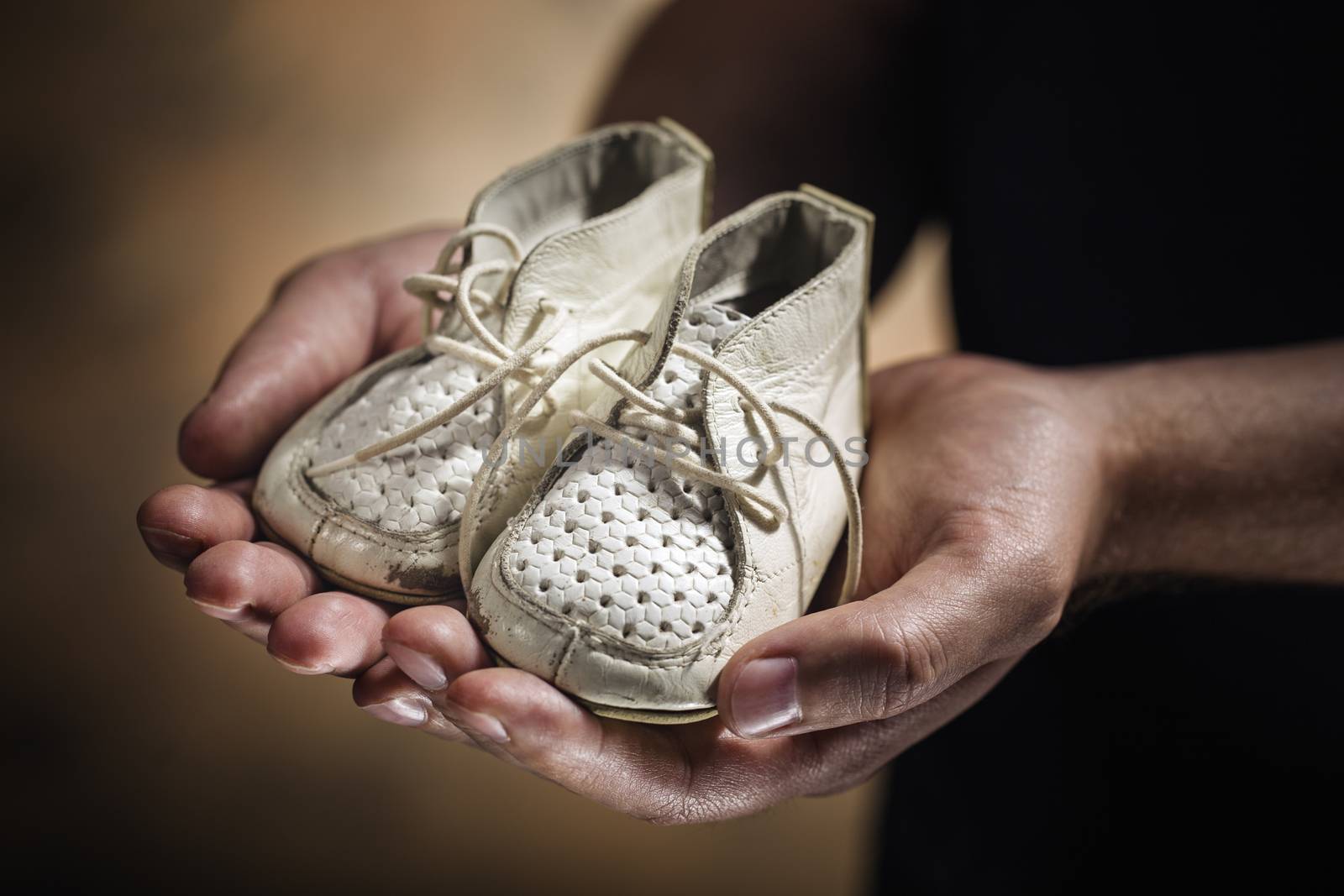 Man holding old and worn leather baby shoes in his hands.